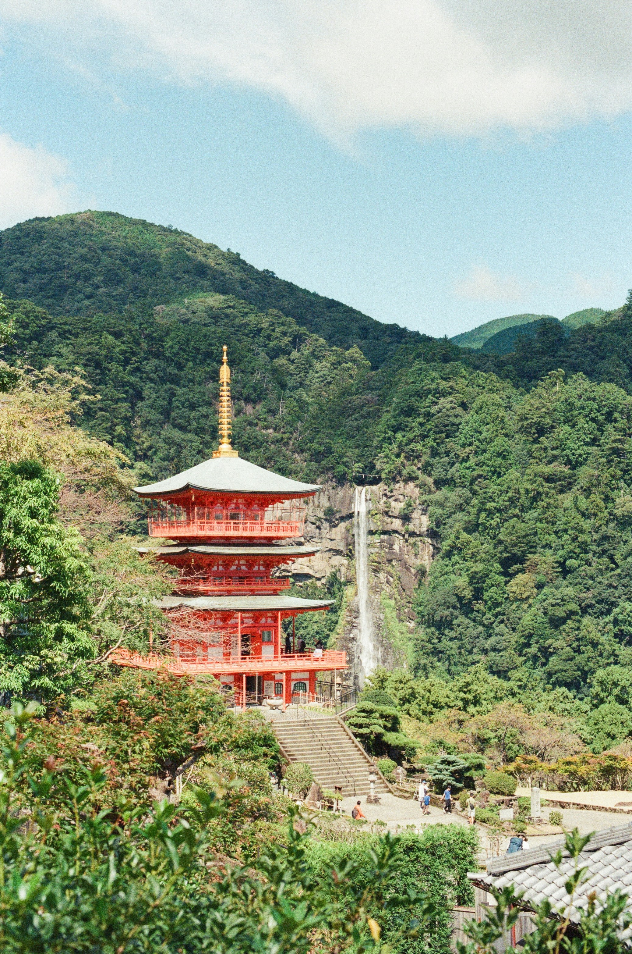 Red pagoda with waterfall and lush green mountains.