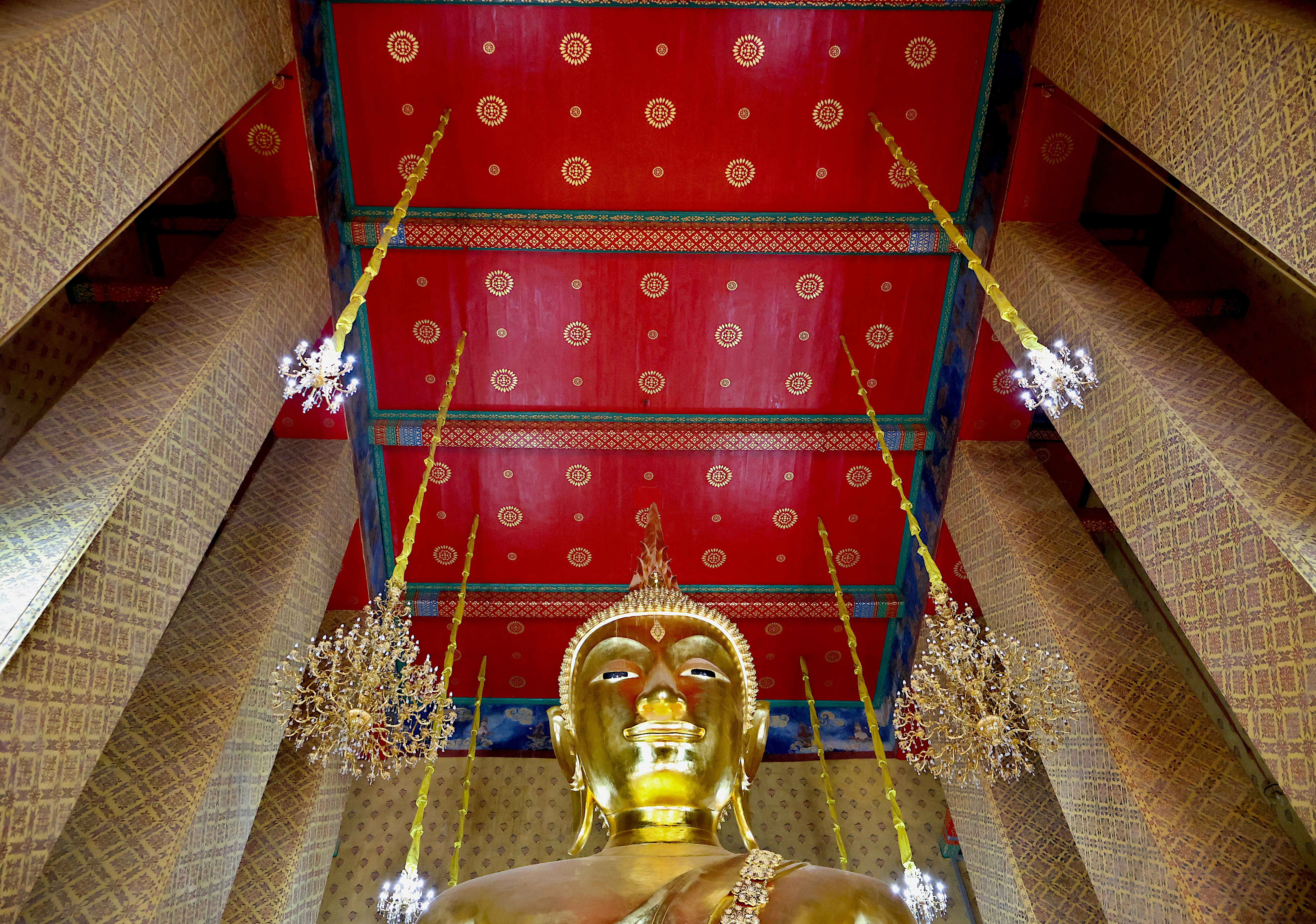 Golden buddha statue inside a temple with red ceiling.