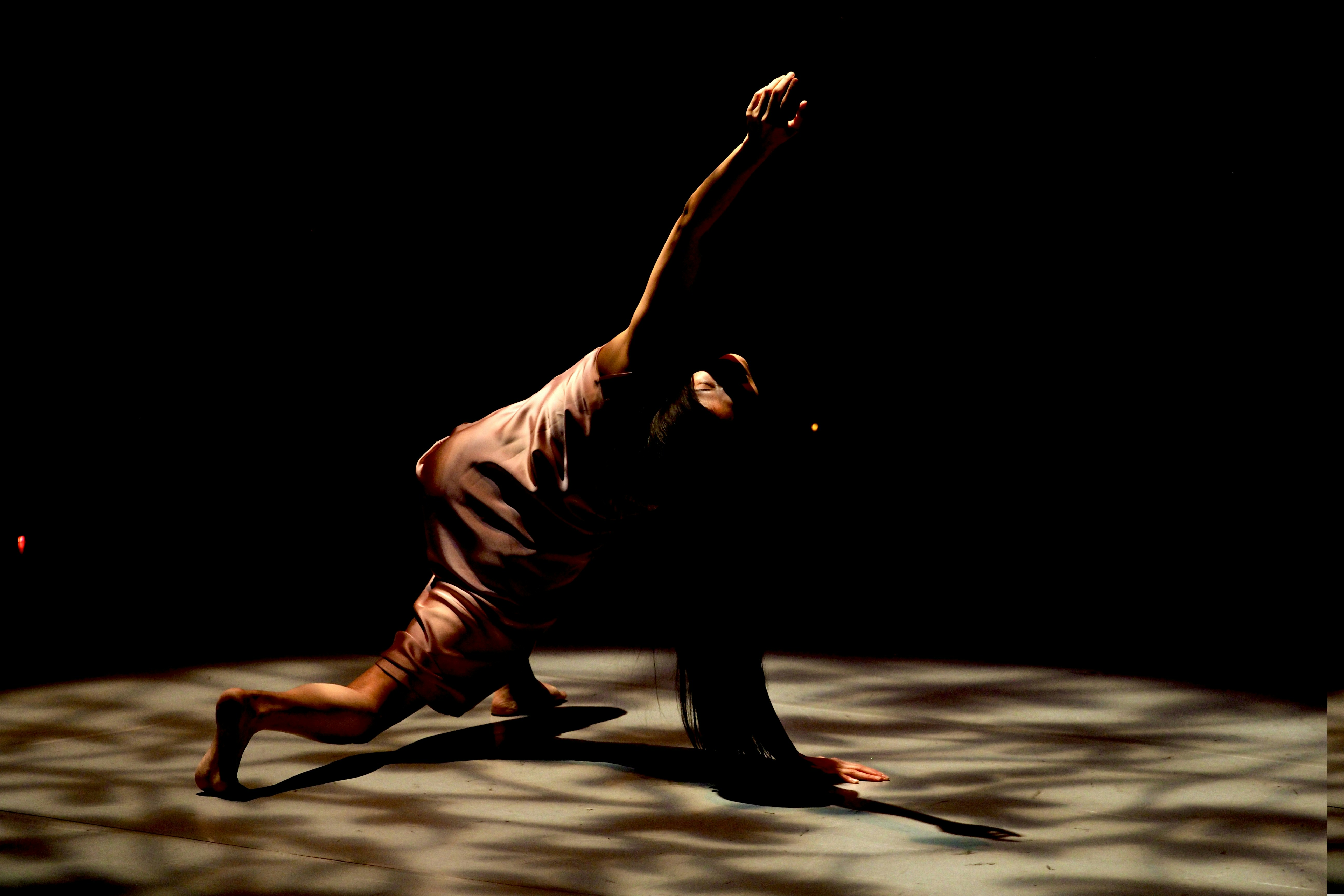 Ein Tänzer nimmt auf einer dunklen Bühne eine dramatische Pose auf.