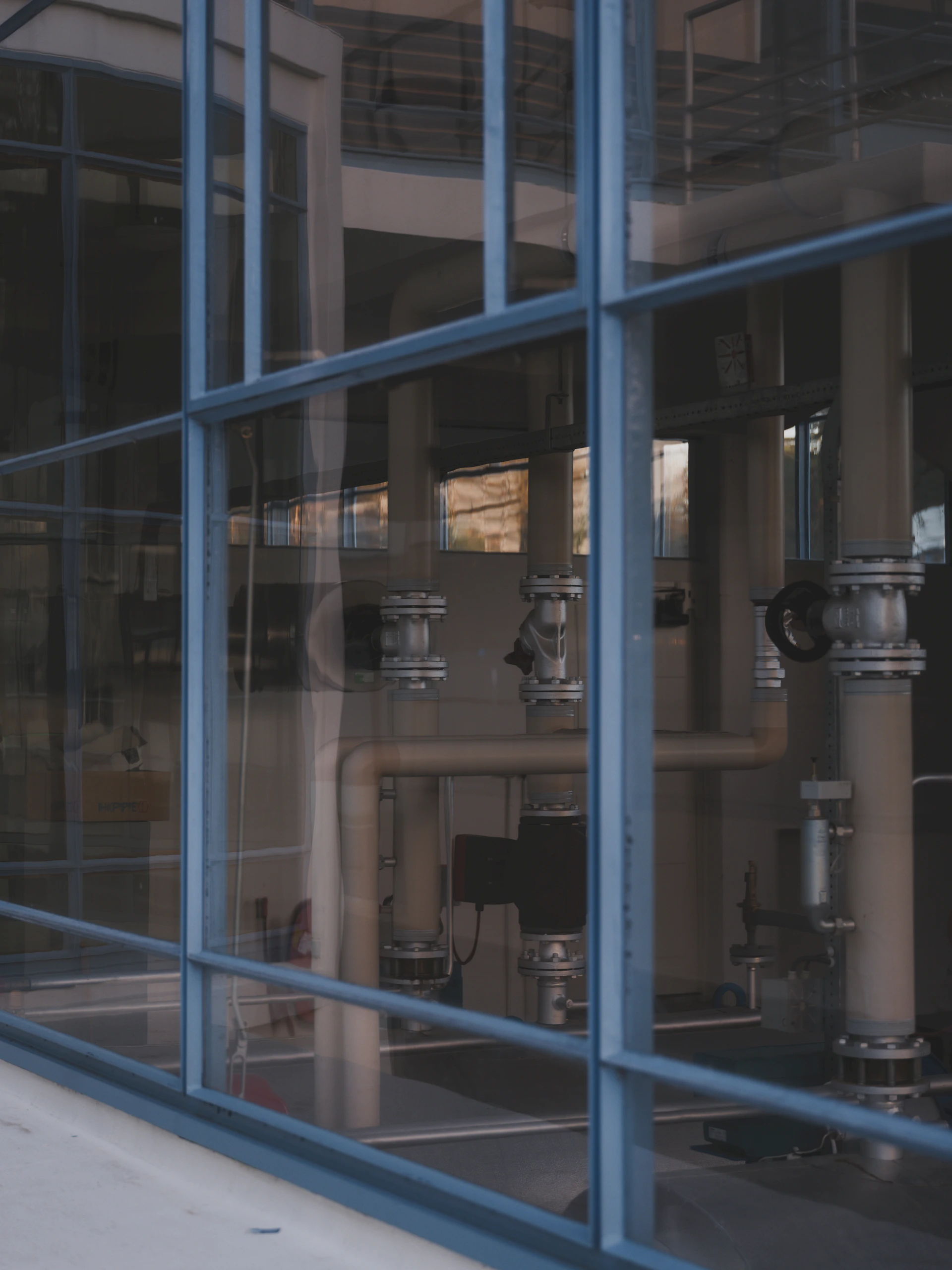 Industrial pipes and valves seen through glass windows