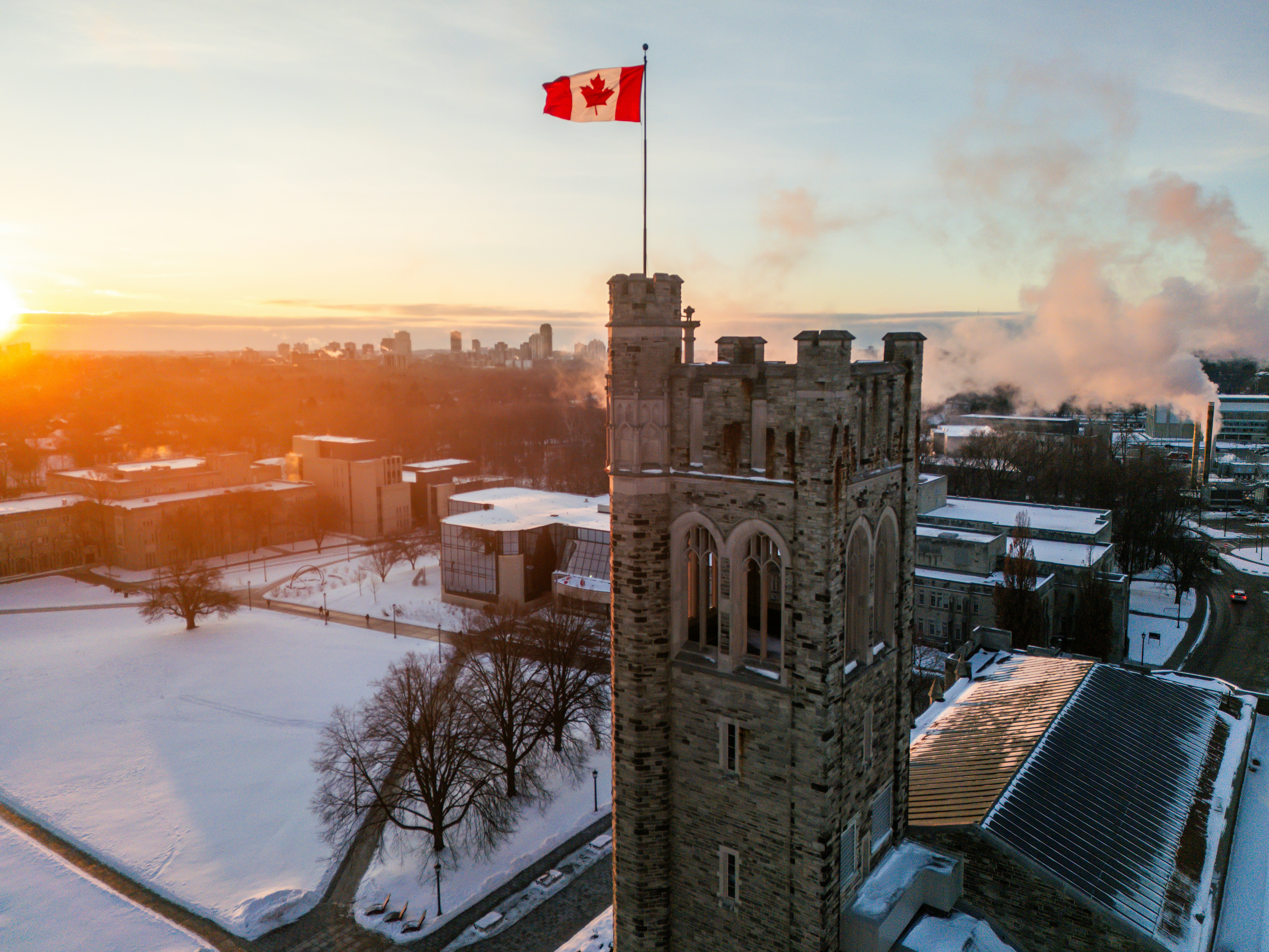 Canadian flag flies atop a stone tower at sunrise.
