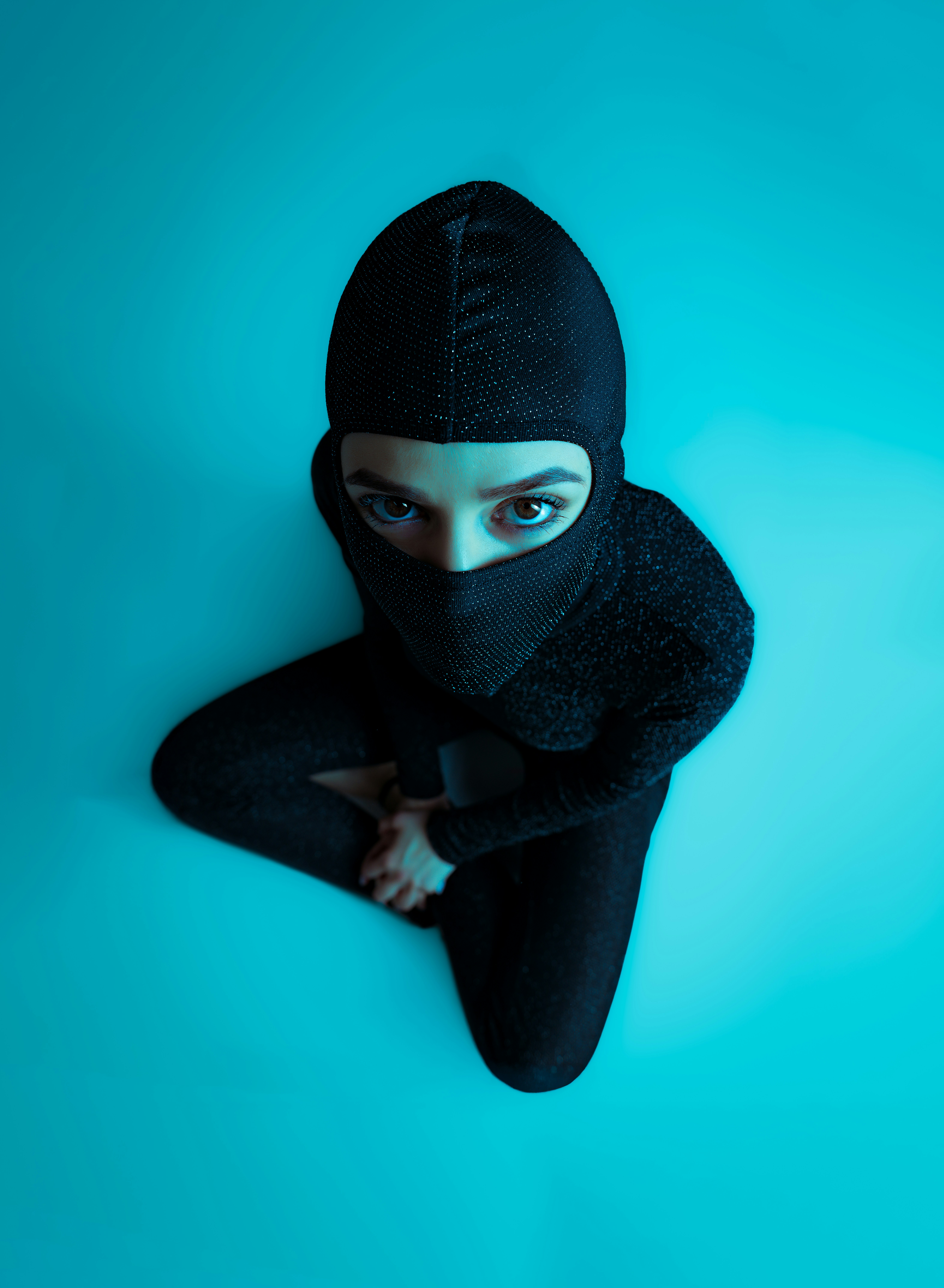 Person in black outfit and mask on blue background