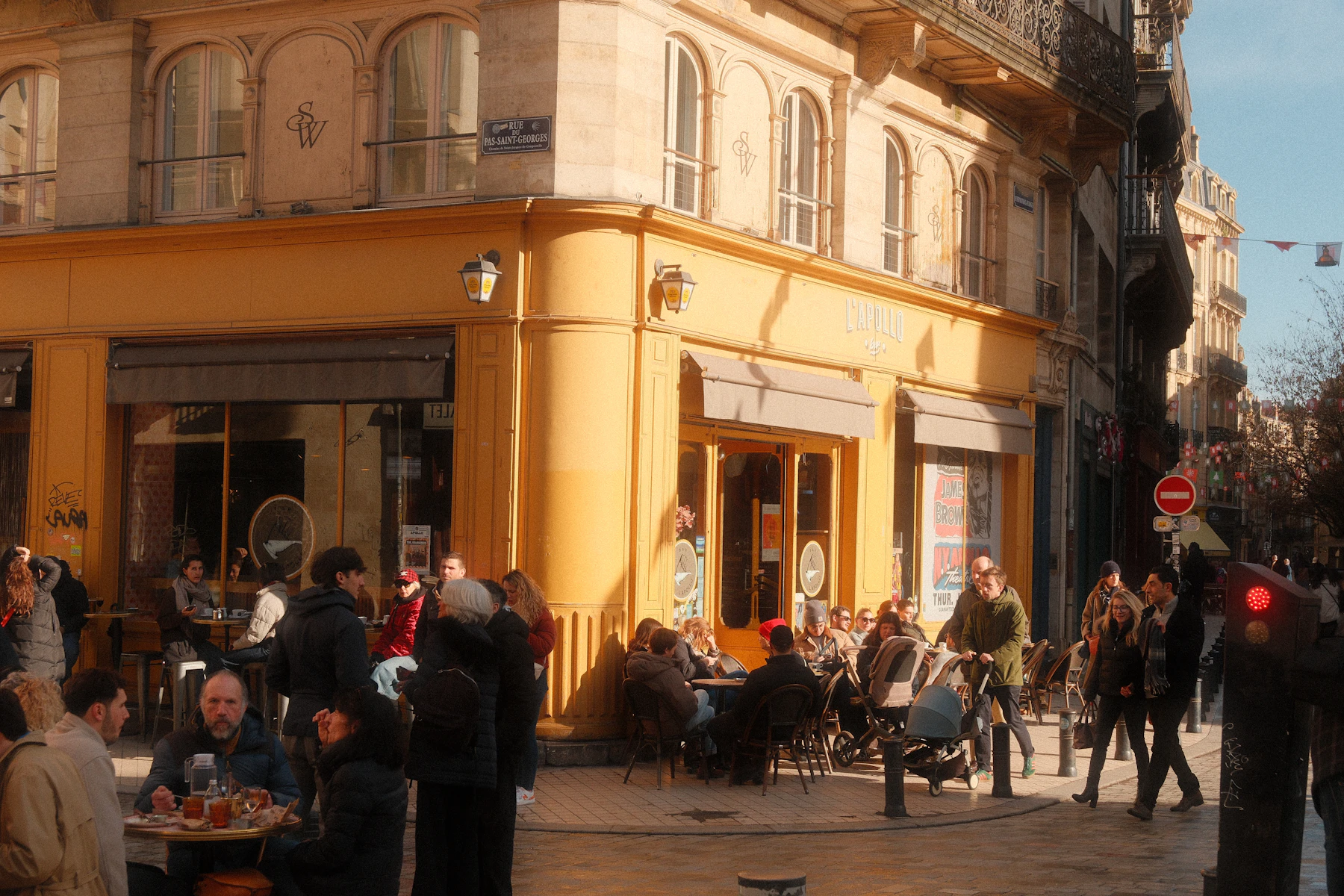 A yellow corner cafe with full sidewalk tables and people passing on the street in front of it