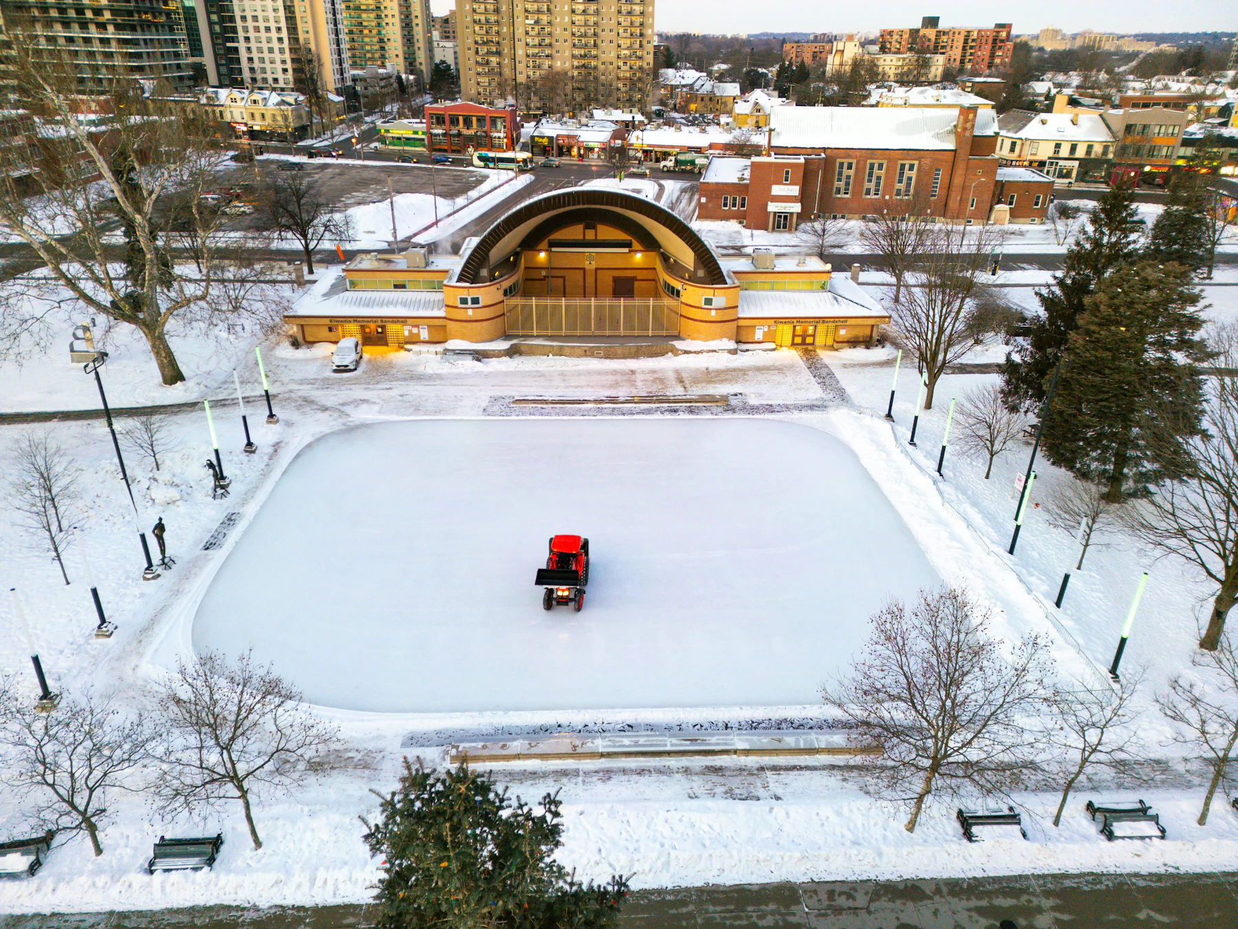 A red resurfacing machine crossing a snow-edged outdoor rink in a park, seen from above