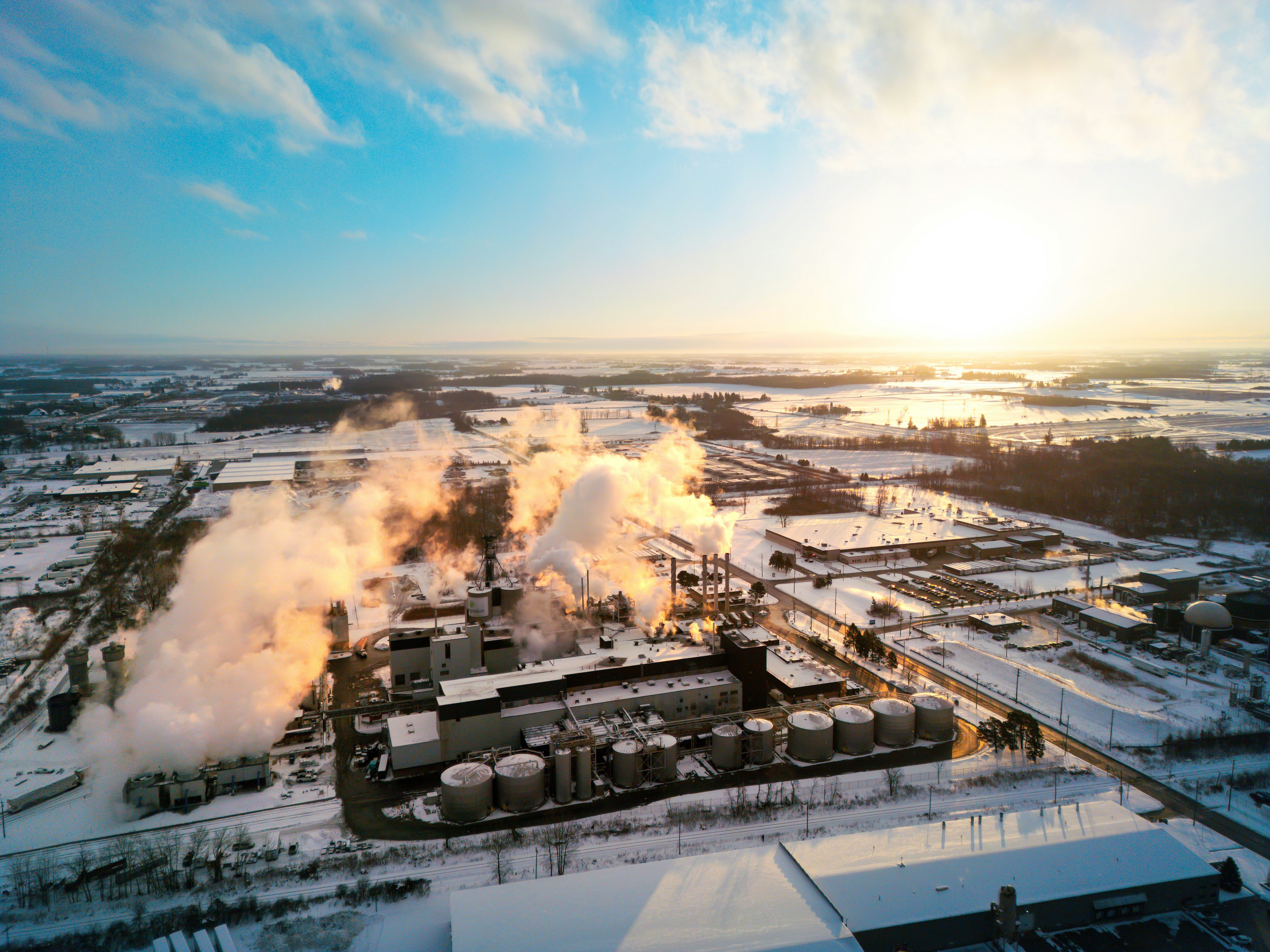 Industrial complex emitting steam on a snowy day.