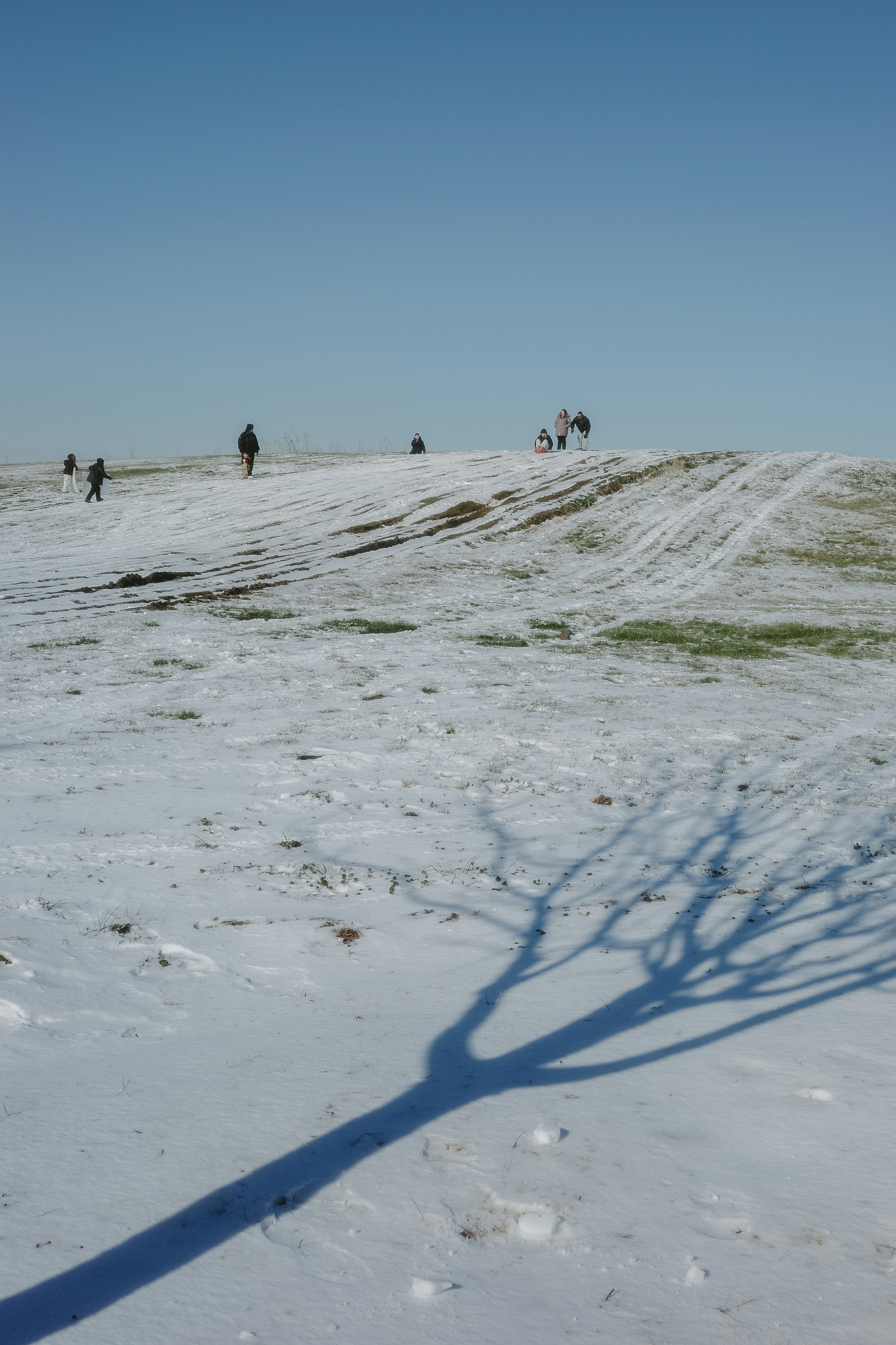 Des gens descendant une colline enneigée sous un ciel dégagé.