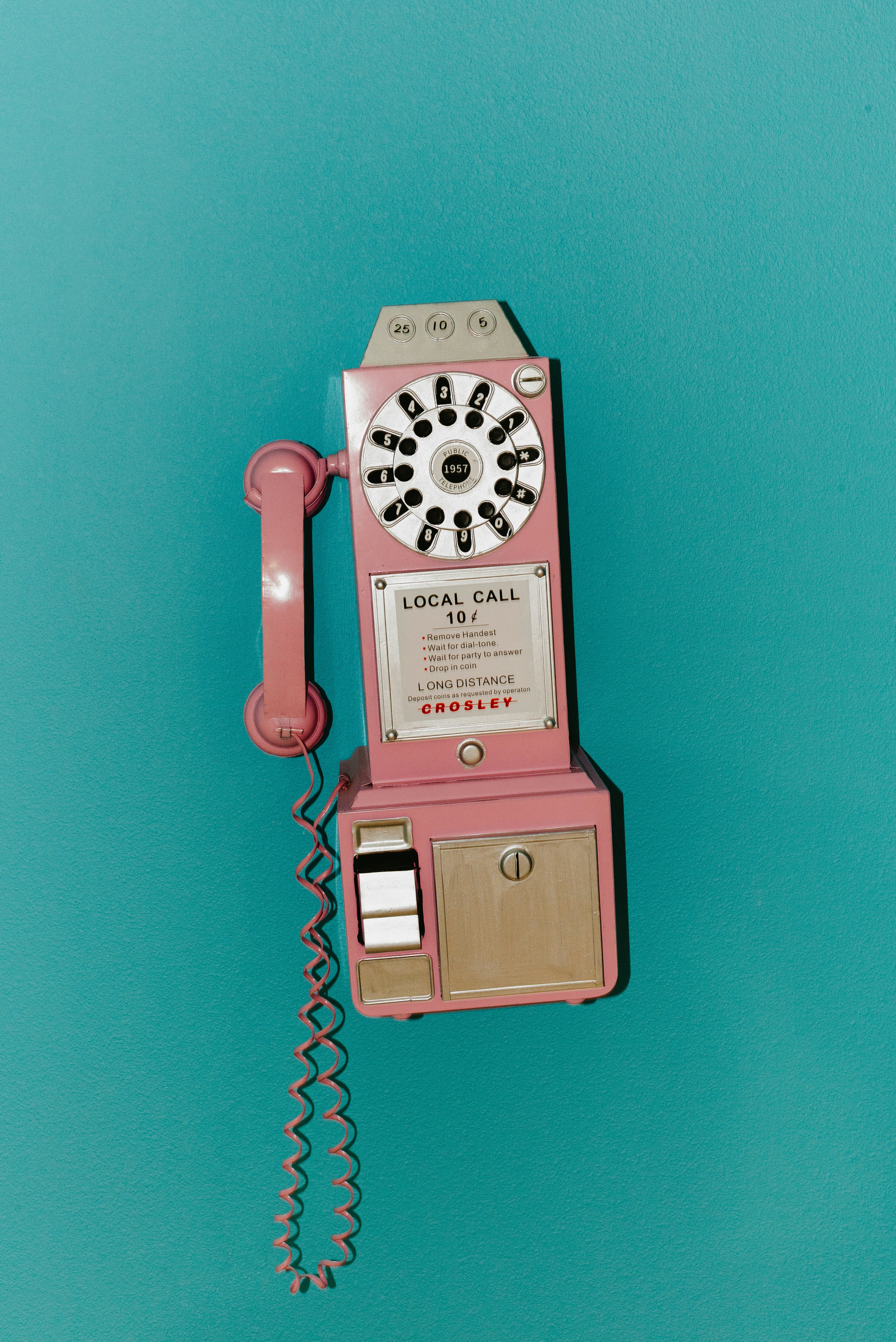A pink vintage payphone mounted on a teal wall
