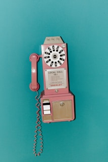 A pink vintage payphone mounted on a teal wall
