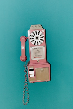 A pink vintage payphone mounted on a teal wall