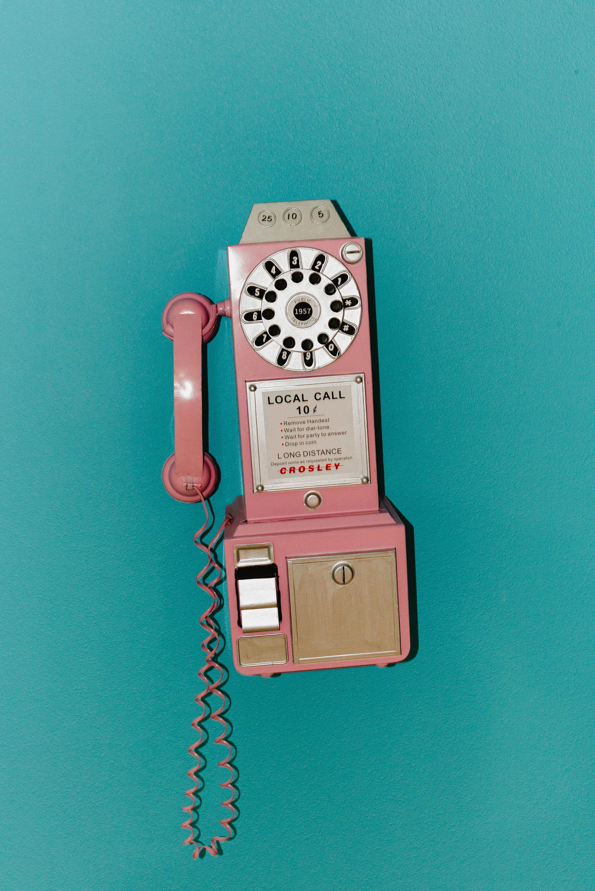 A pink vintage payphone mounted on a teal wall
