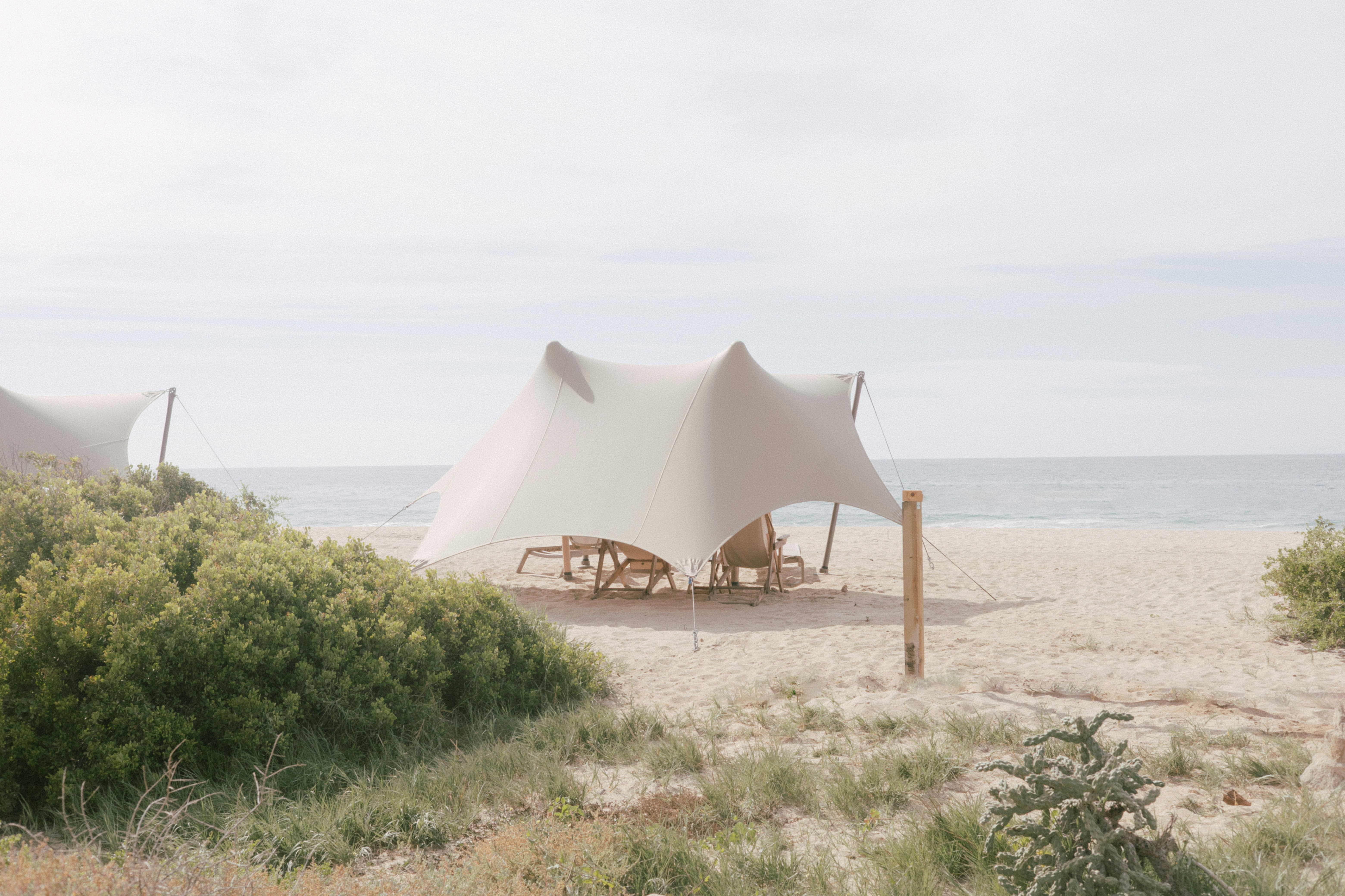Zwei Zelte aus Segeltuch stehen an einem Sandstrand.