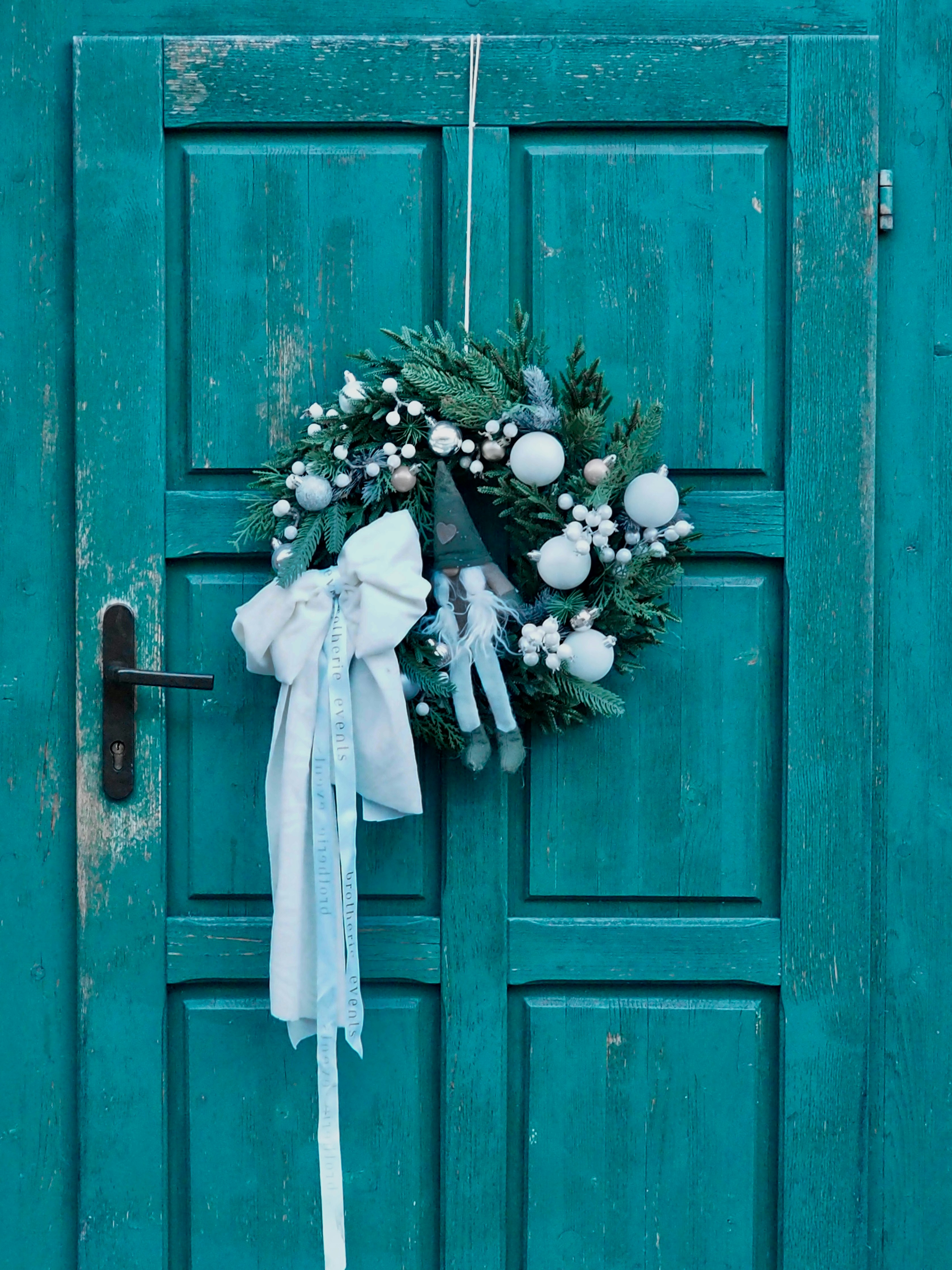 A festive wreath hangs on a weathered teal door.