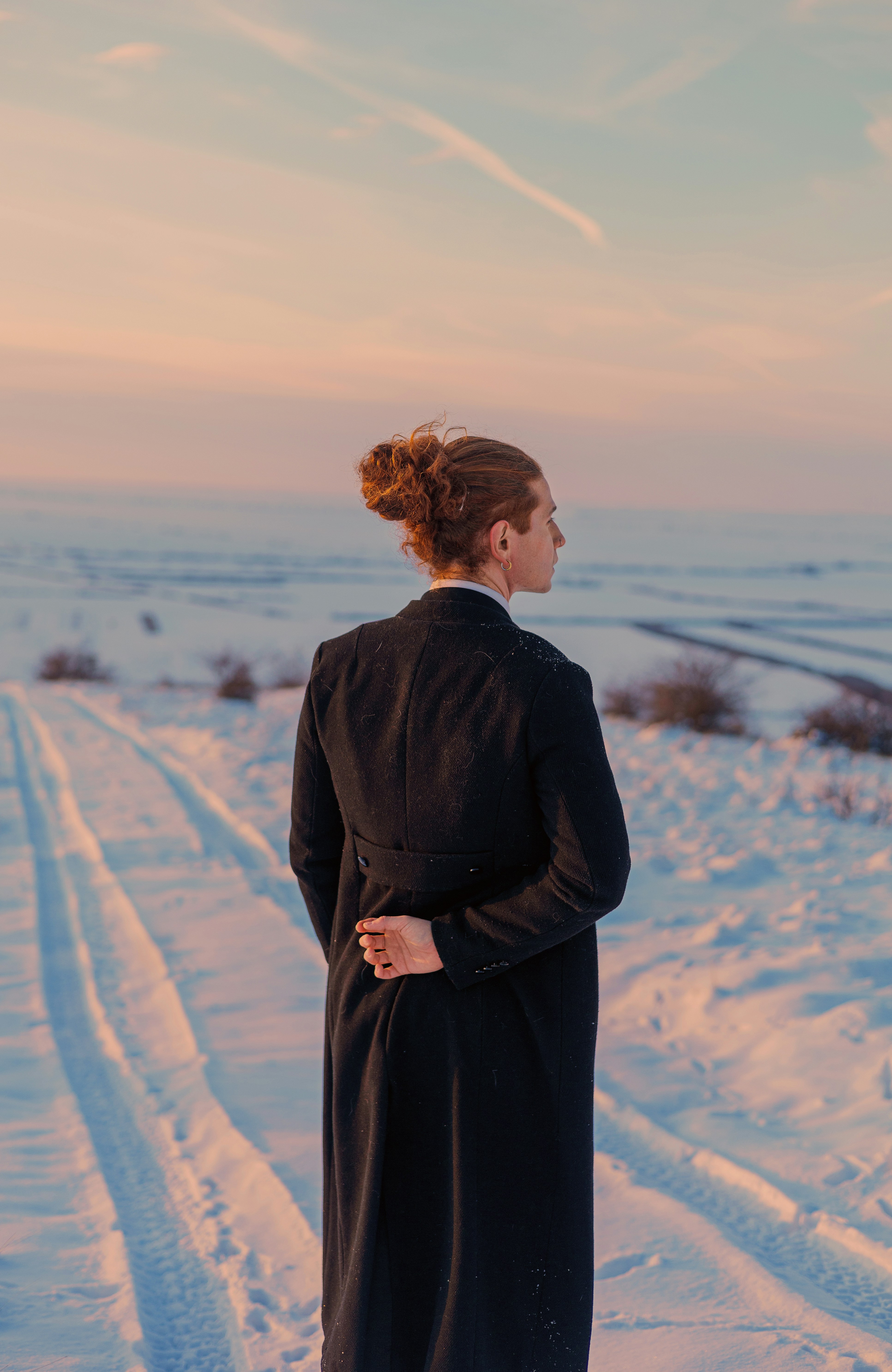 Mulher de casaco preto em pé em uma paisagem nevada ao pôr do sol