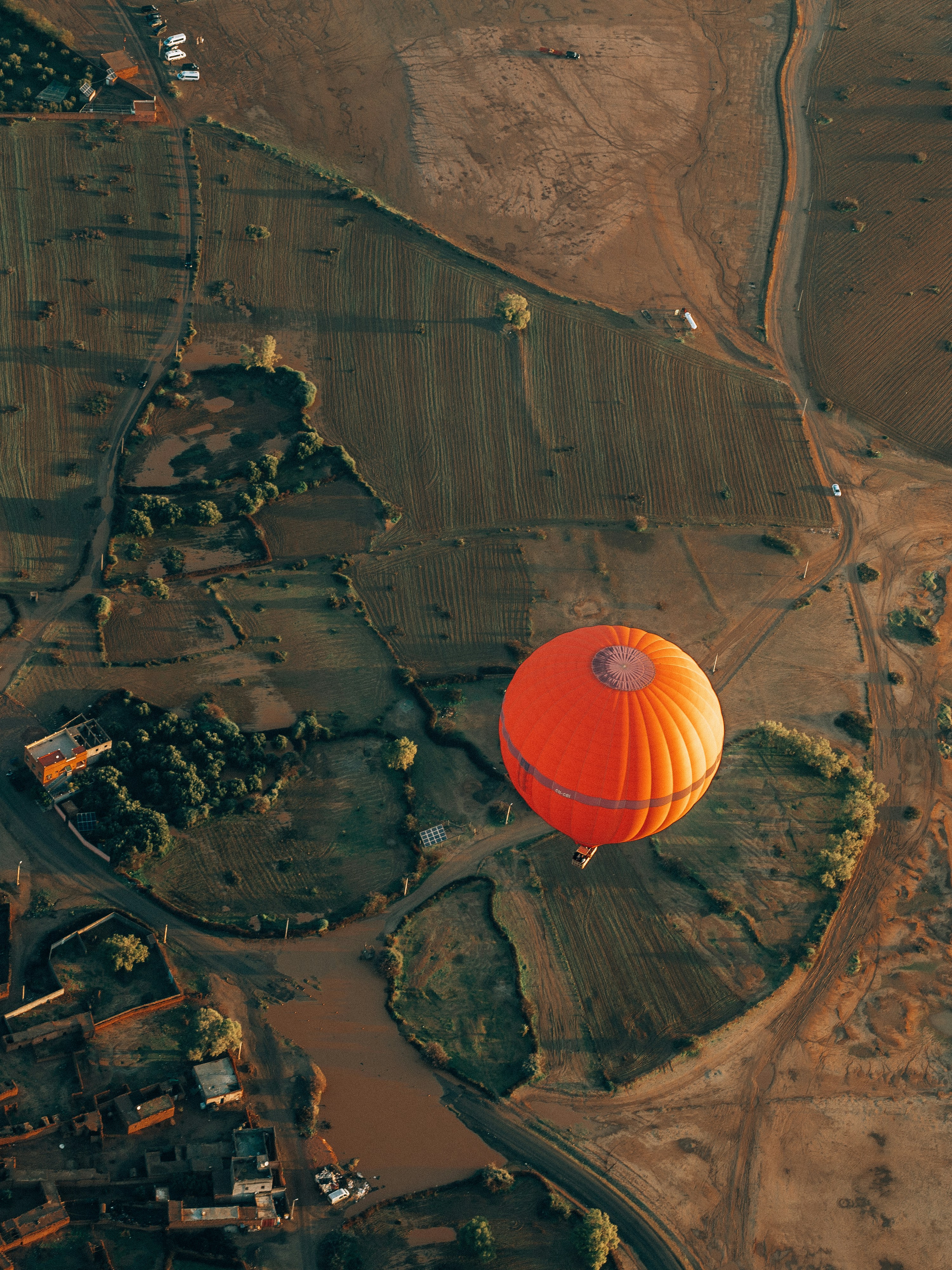 Una mongolfiera arancione fluttua sopra un paesaggio rurale.