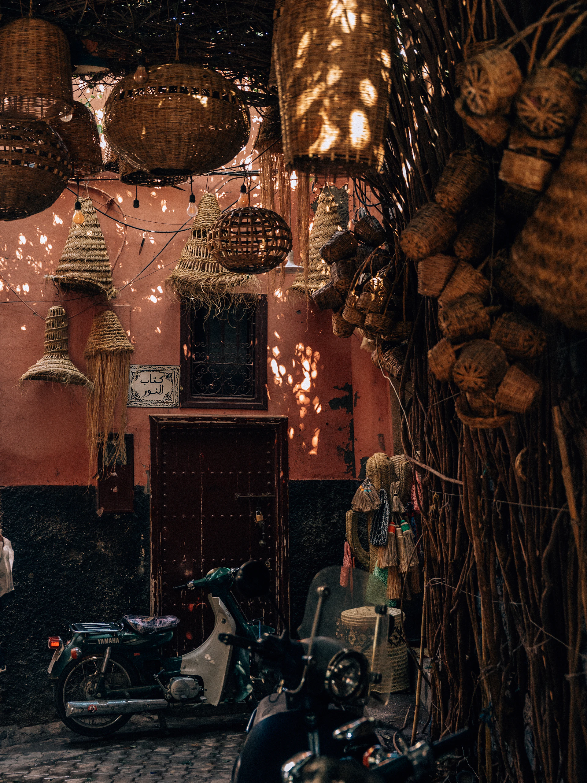 Woven lanterns hanging in a warm terracotta-walled Marrakech medina alley