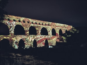 Ancient aqueduct illuminated with colorful patterns at night