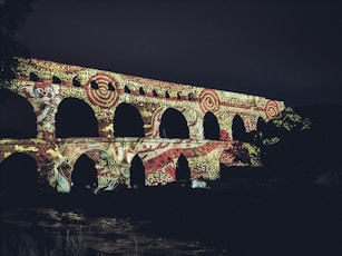 Ancient aqueduct illuminated with colorful patterns at night