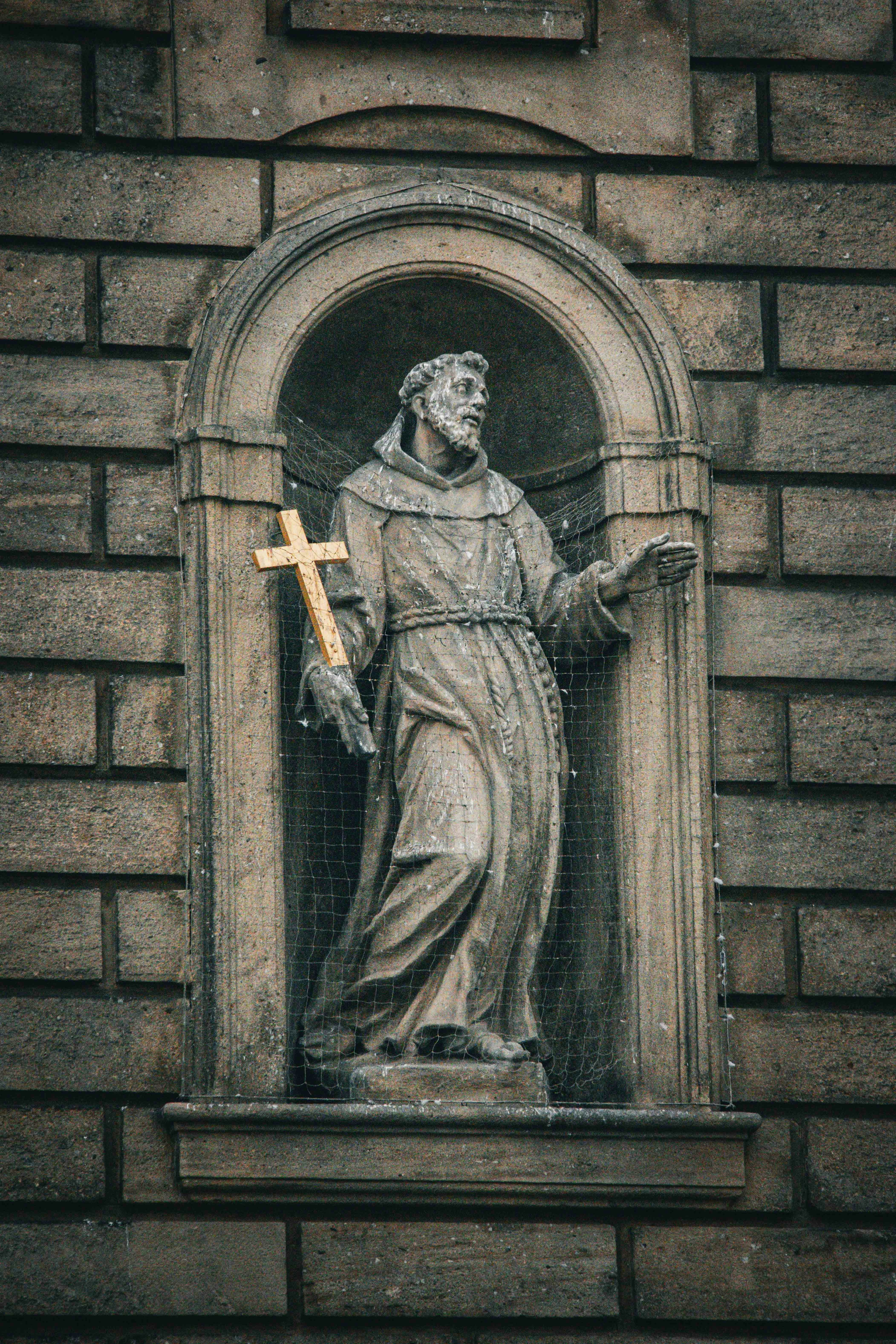 Estatua de piedra de un monje sosteniendo una cruz dorada.