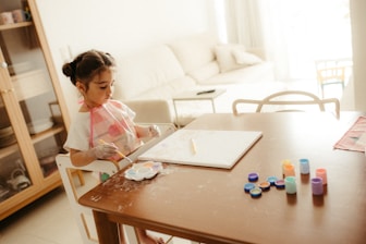 Young girl painting at a table with colorful paints.