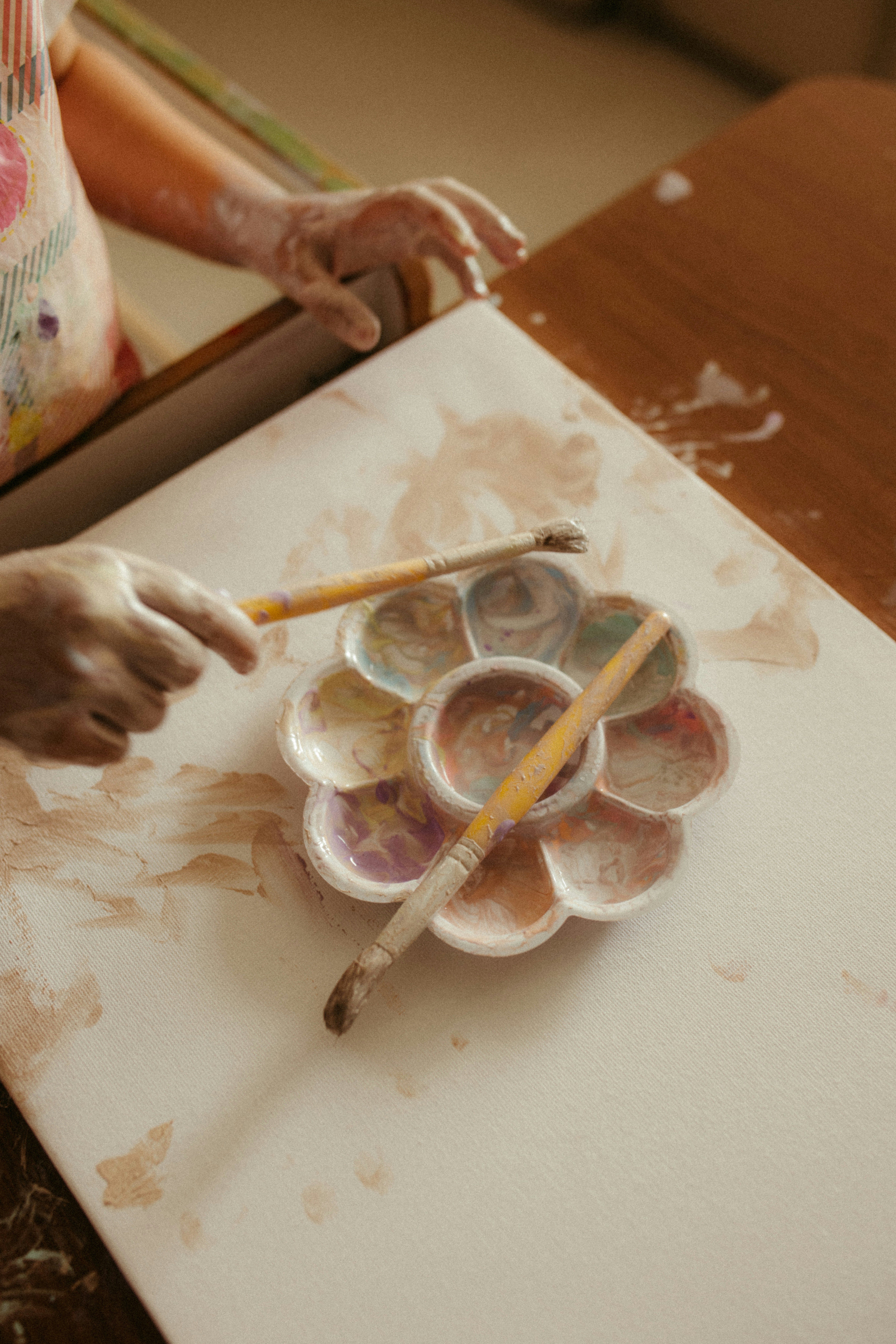 Artist's hands holding brushes over paint palette.