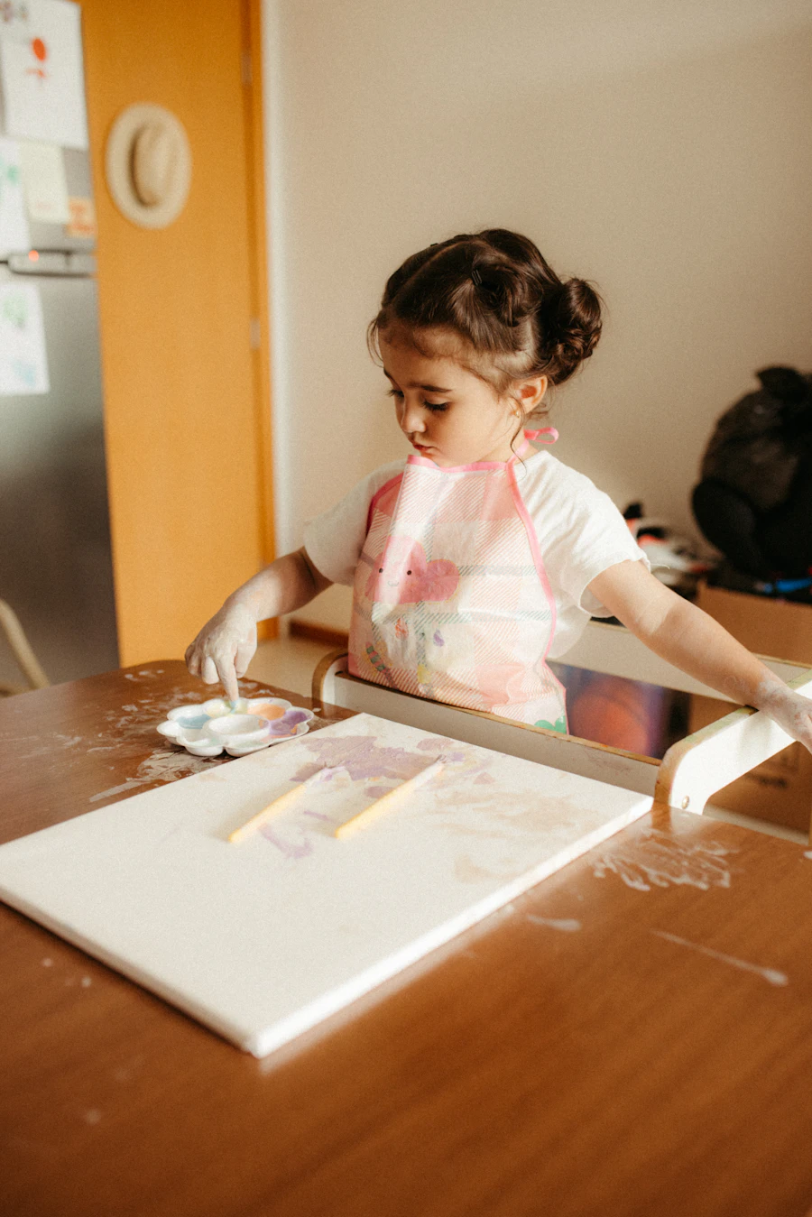 A young girl paints on a canvas at a small wooden table