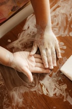Child's hands covered in white paint on a wooden table.