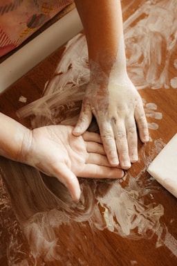 Child's hands covered in white paint on a wooden table.