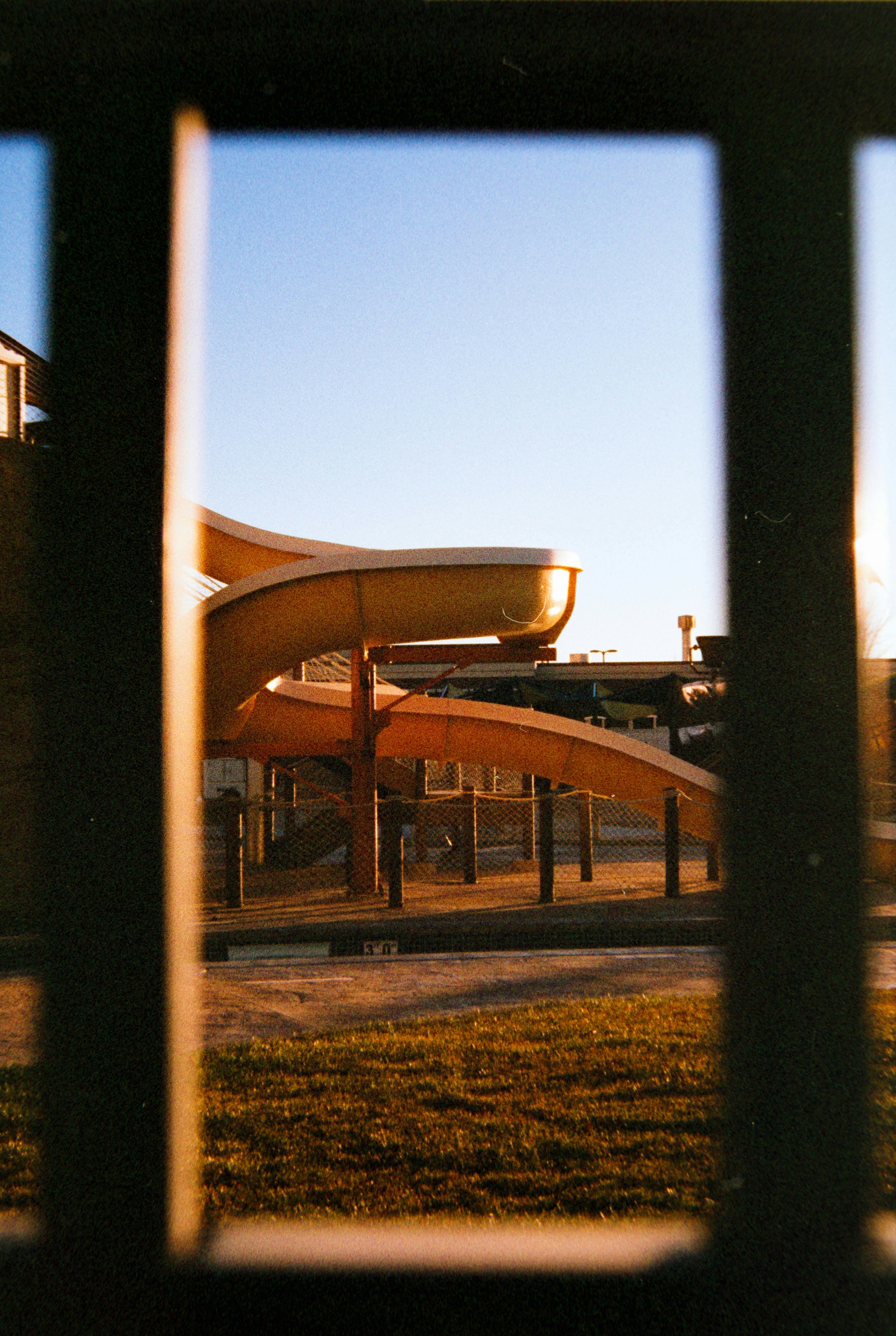 A yellow playground slide seen through a fence.