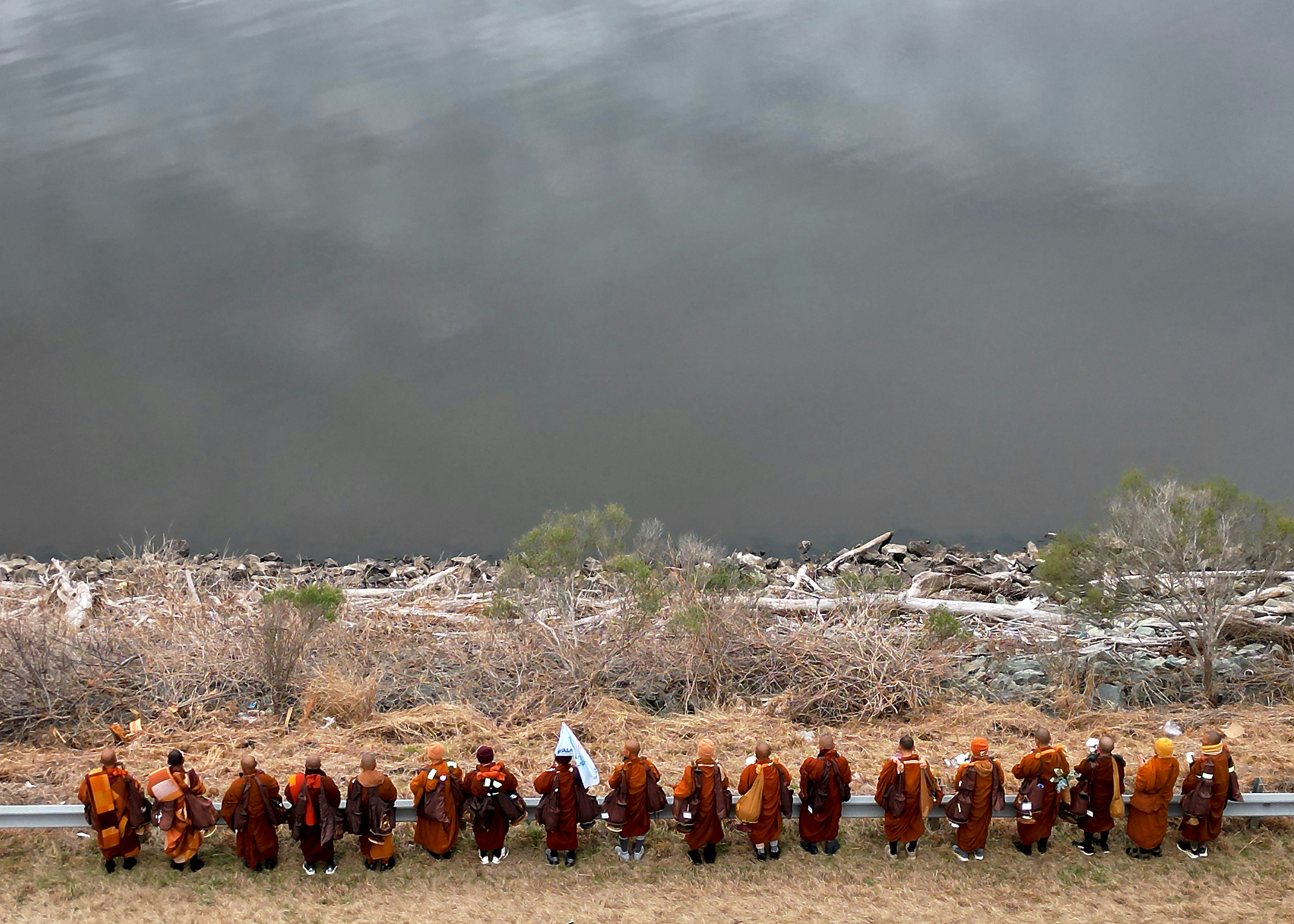 Monks in orange robes holding hands by water