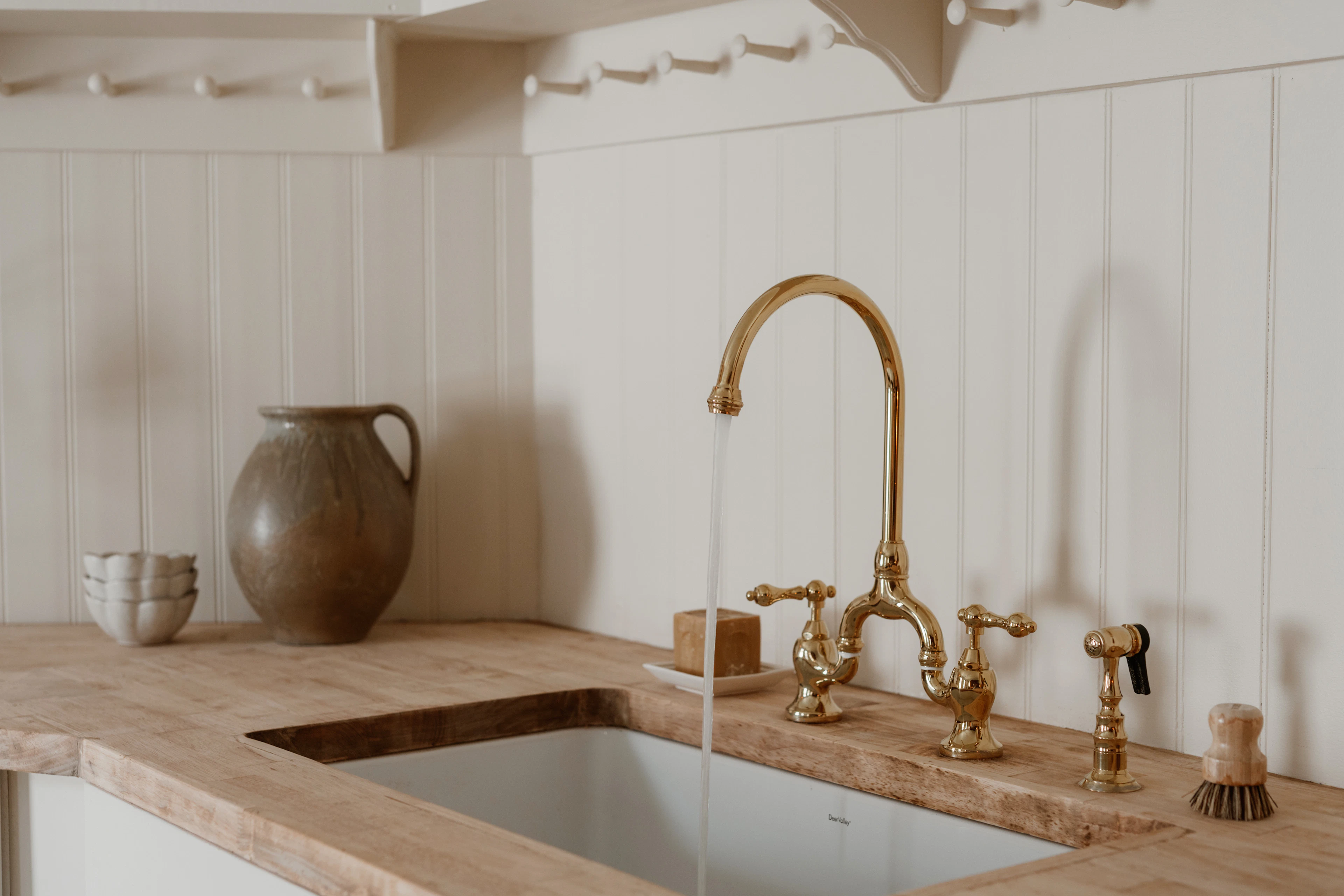 Unlacquered brass bridge tap over a stone sink with a timber worktop