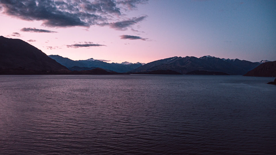 Serene lake surrounded by majestic mountains at sunset with vibrant purple and pink sky