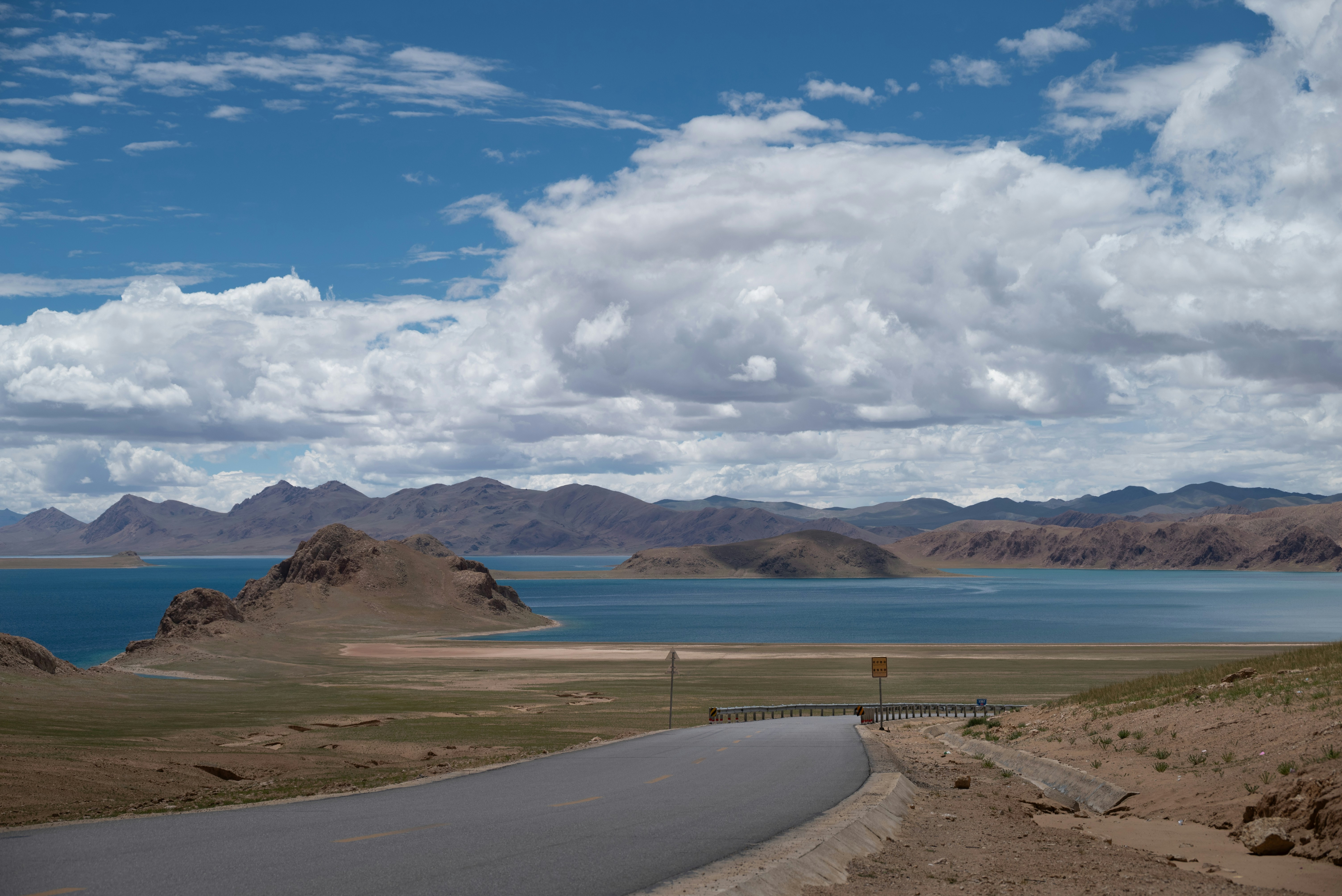 Une route sinueuse mène à un vaste lac et à des montagnes.
