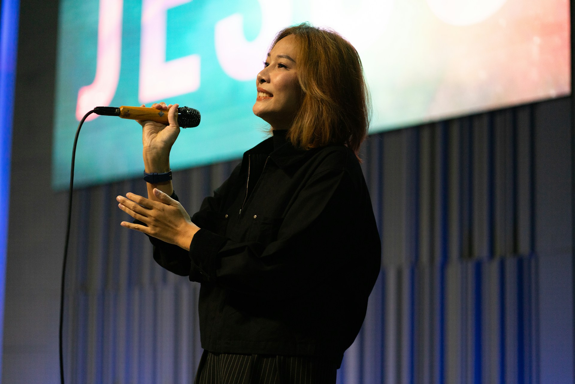 A woman sings into a microphone on stage.
