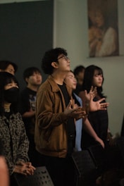 Young adults gathered, looking upwards with hands raised.