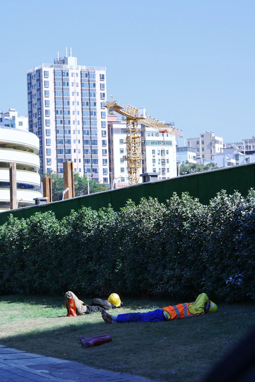 Construction workers resting on grass with buildings behind