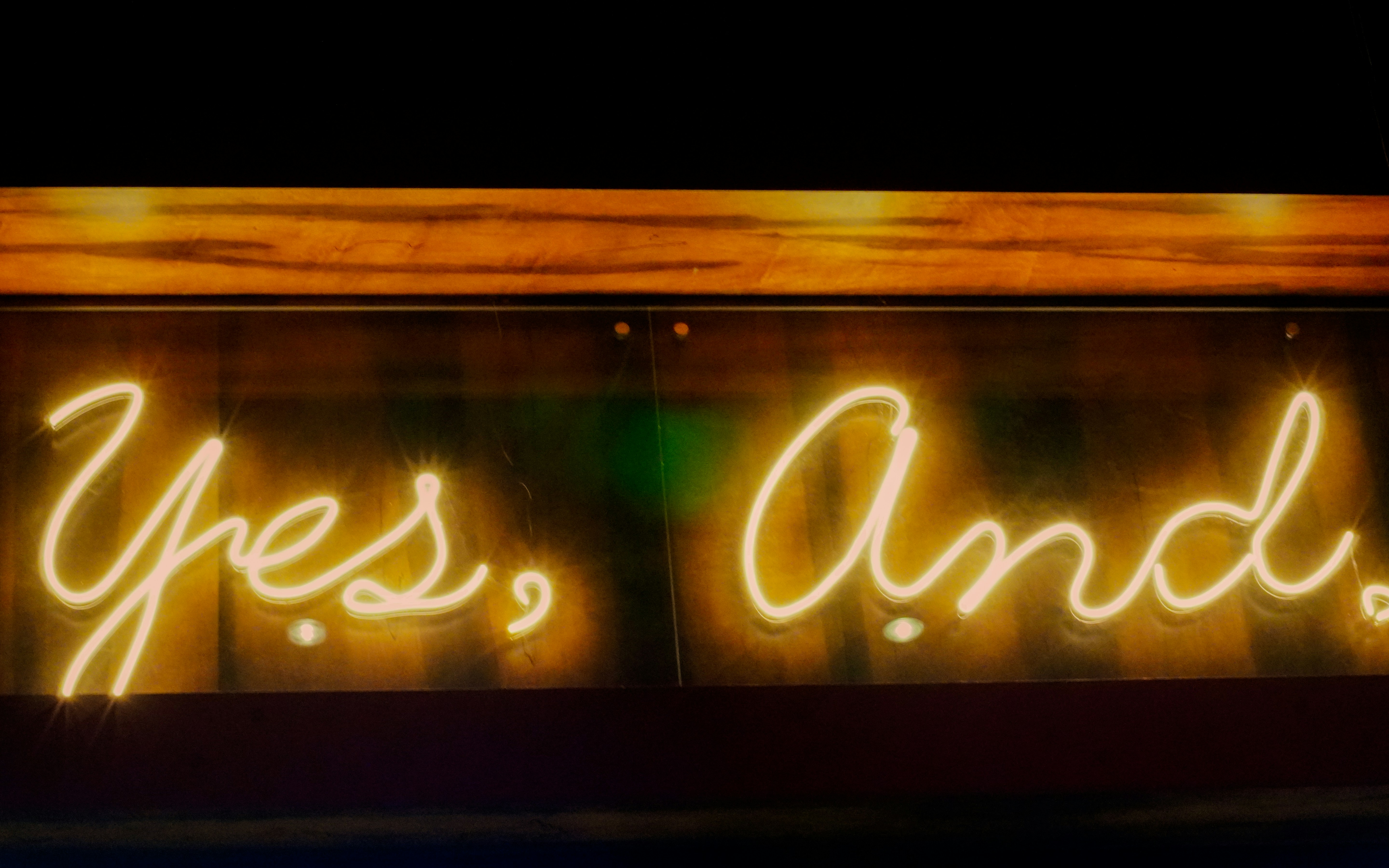 Yellow neon sign reads "yes, and."