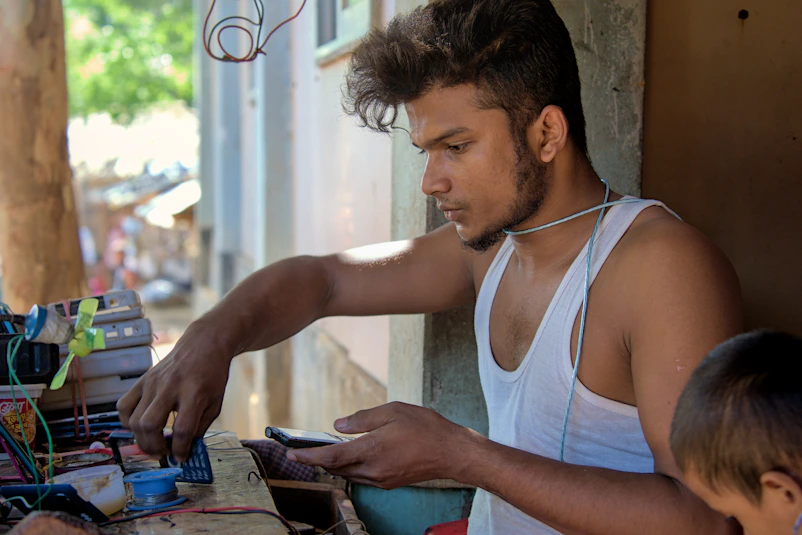 Young man working with electronics at a cluttered desk.