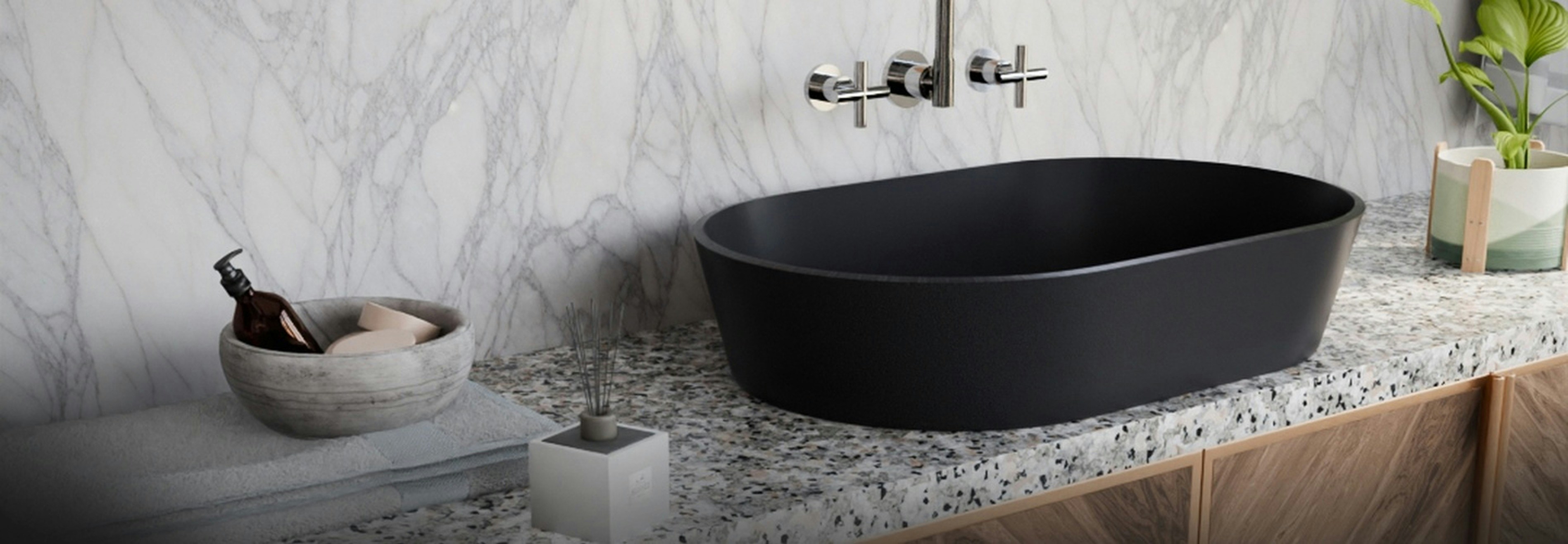 A sophisticated matte-black oval washbasin rests on a textured stone countertop, complemented by a wall-mounted chrome faucet. The white marble backsplash, warm wooden cabinetry, and subtle décor accents create a balanced blend of luxury, minimalism, and contemporary design, perfect for high-end modern bathrooms.