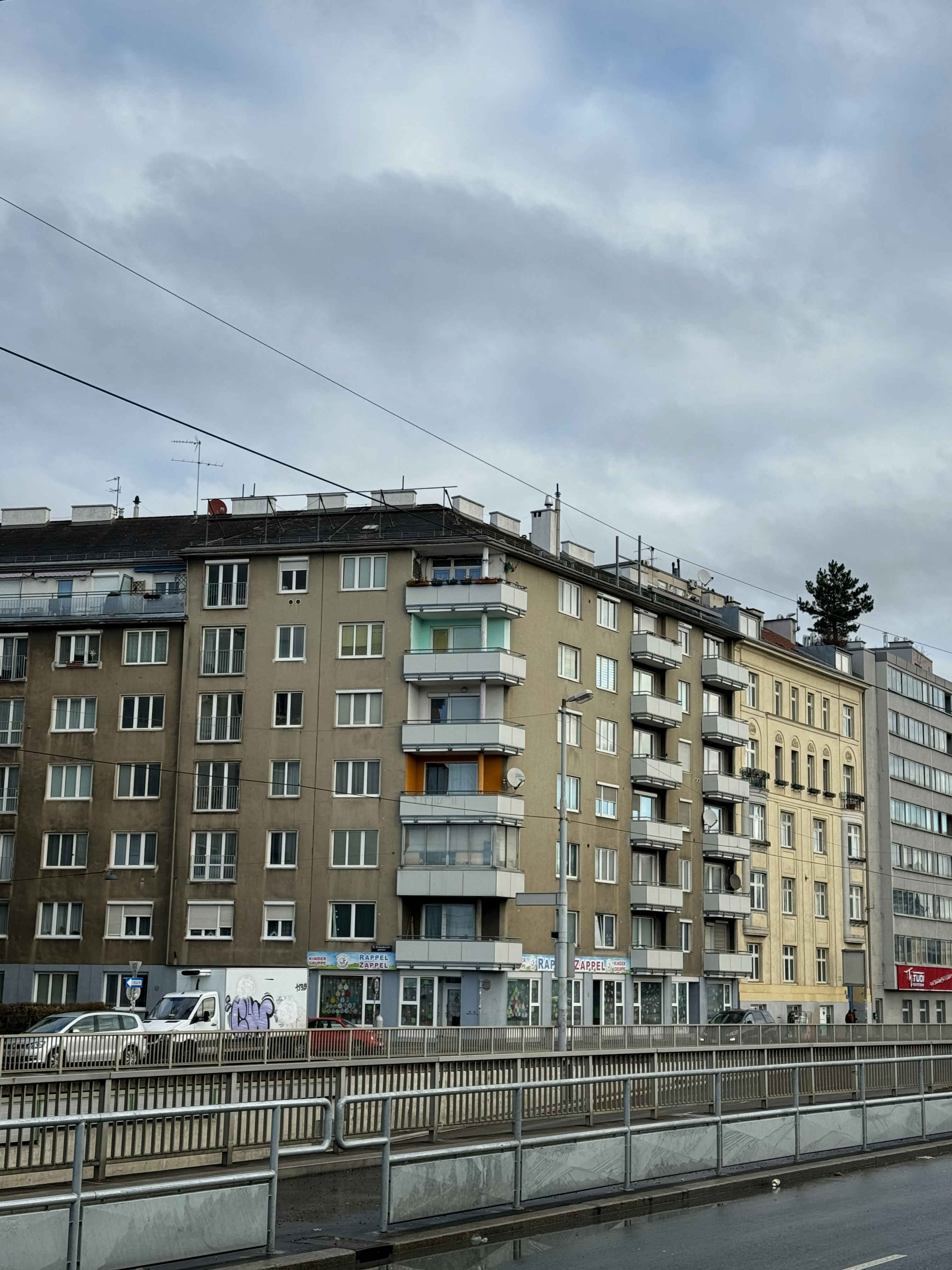 Apartment buildings line a street under cloudy skies.