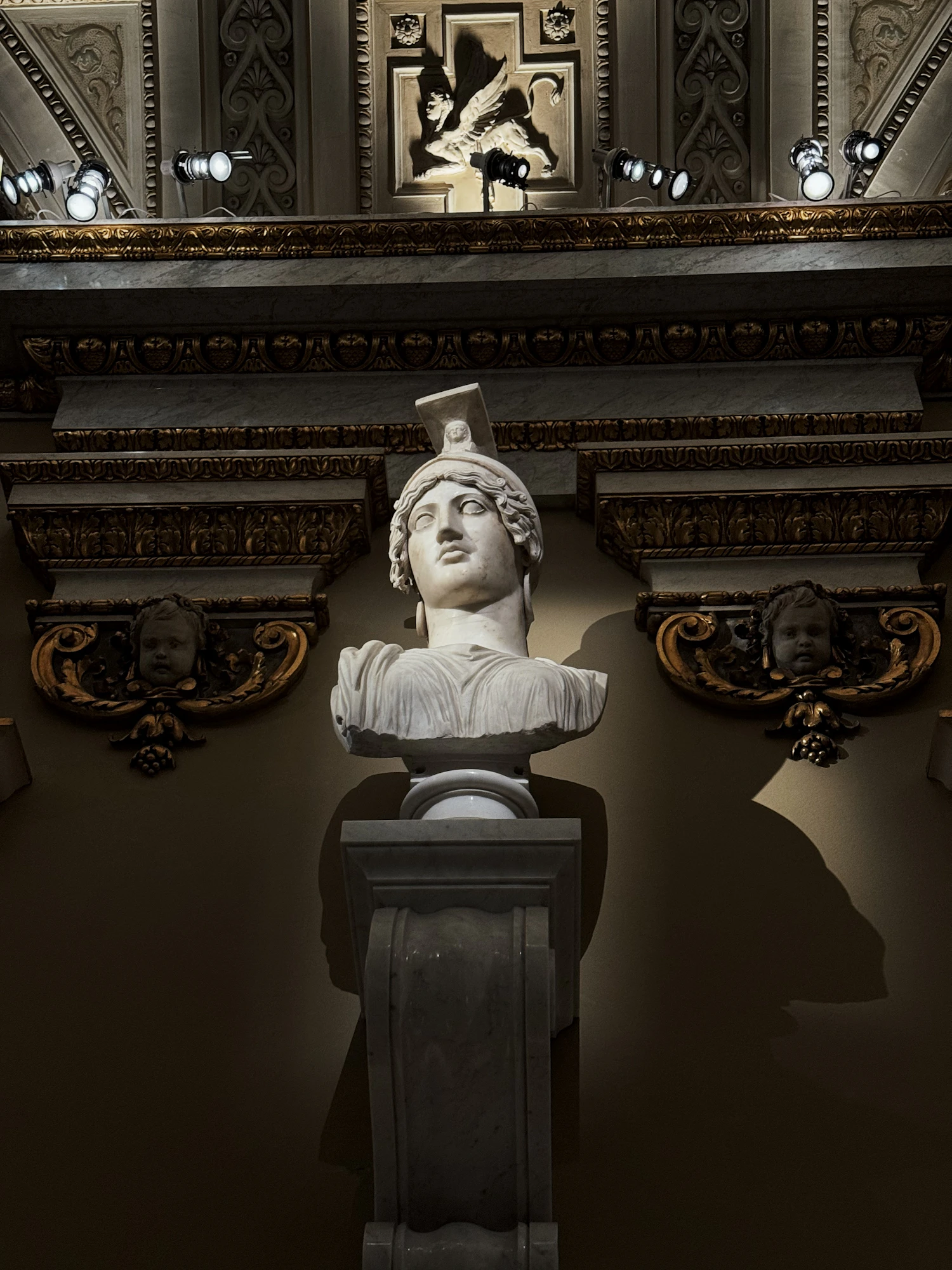 A marble head wearing a helmet, lit from one side in a darkened room