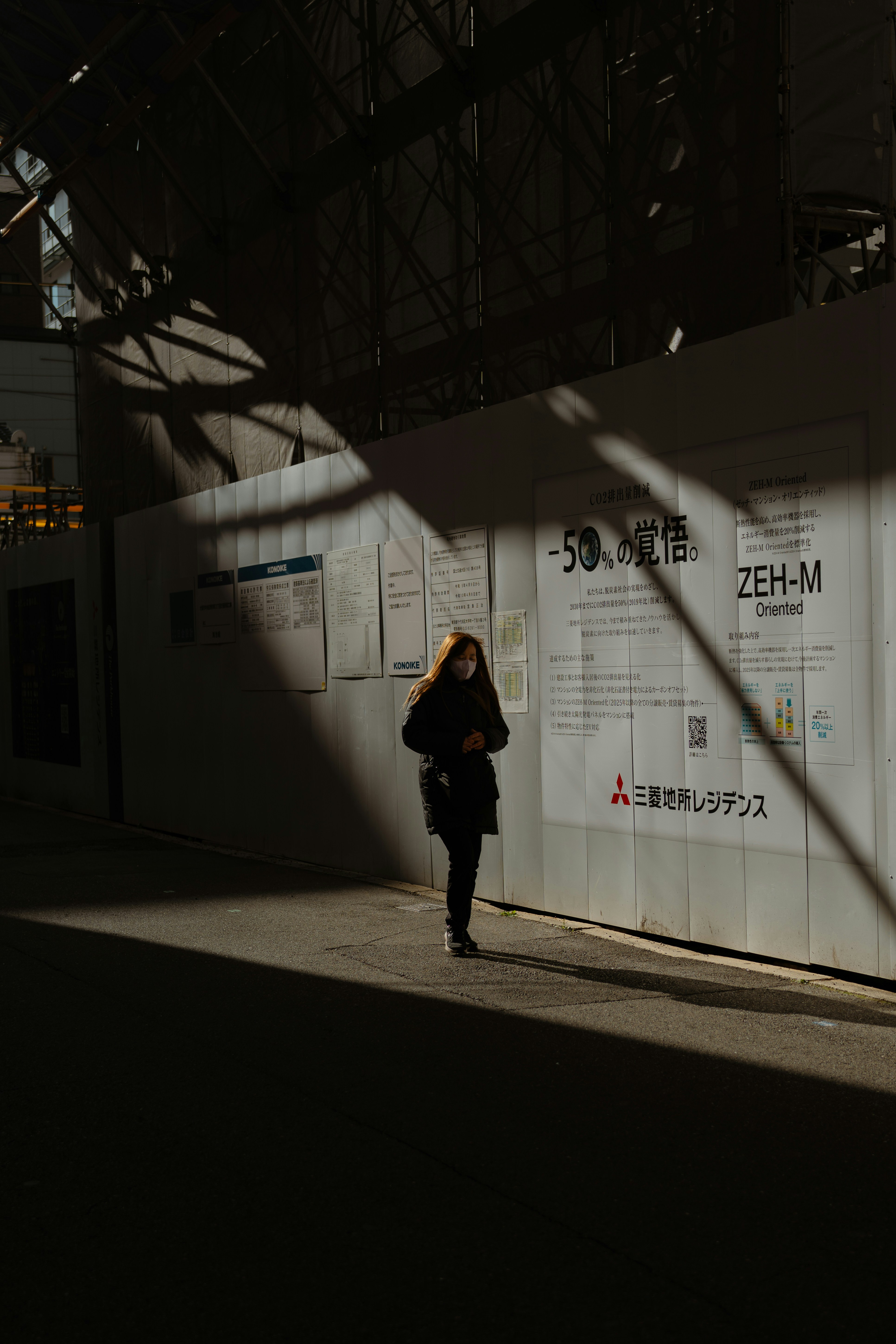 Woman standing in sunlight near construction wall.
