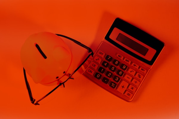 A piggy bank and calculator on an orange background.