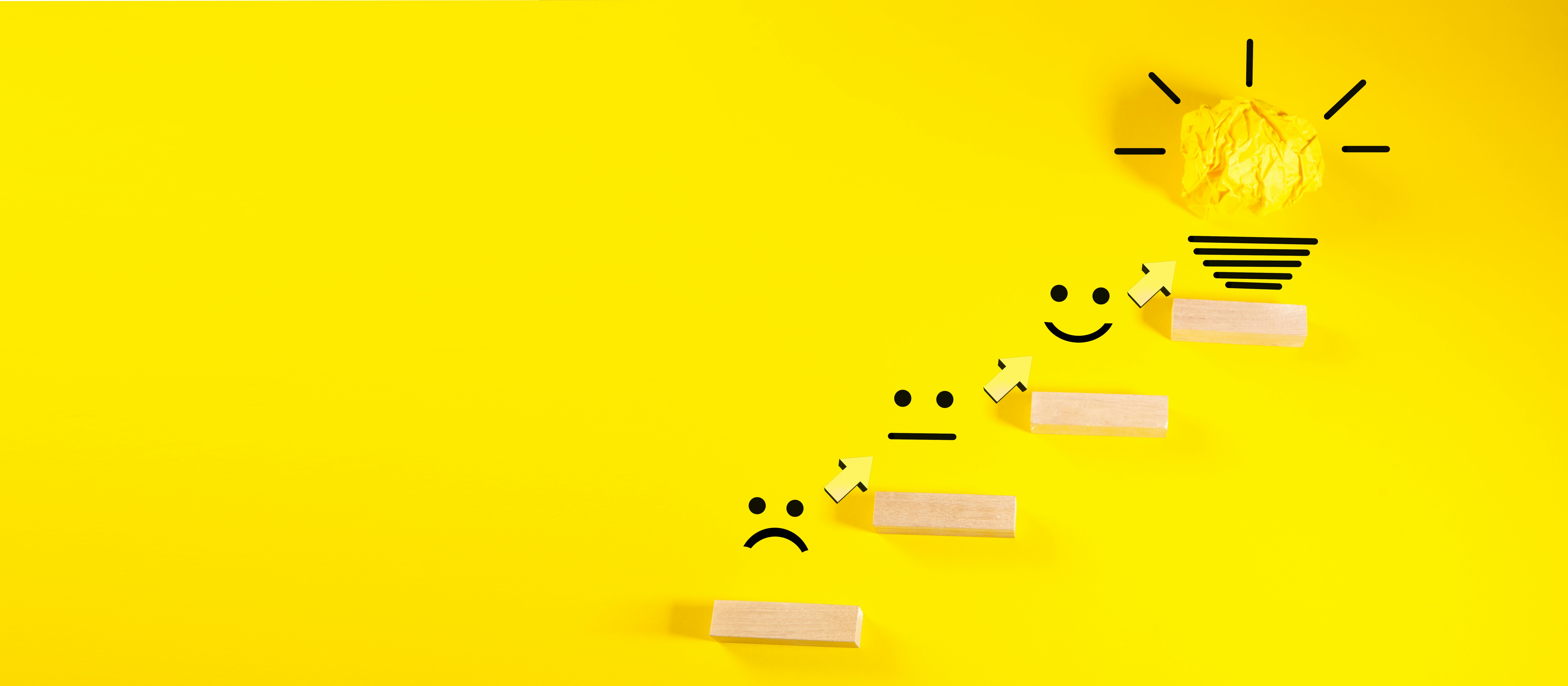 Wooden blocks with smiley faces ascending towards a lightbulb.