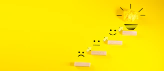Wooden blocks with smiley faces ascending towards a lightbulb.