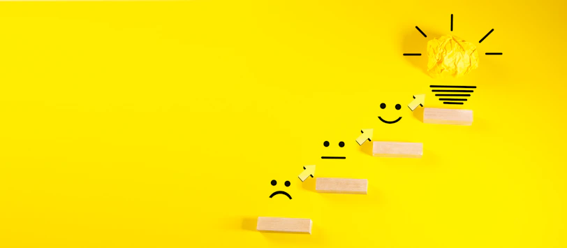 Wooden blocks with smiley faces ascending towards a lightbulb.