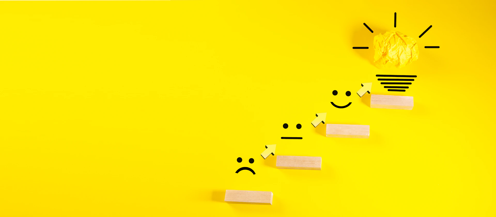 Wooden blocks with smiley faces ascending towards a lightbulb.