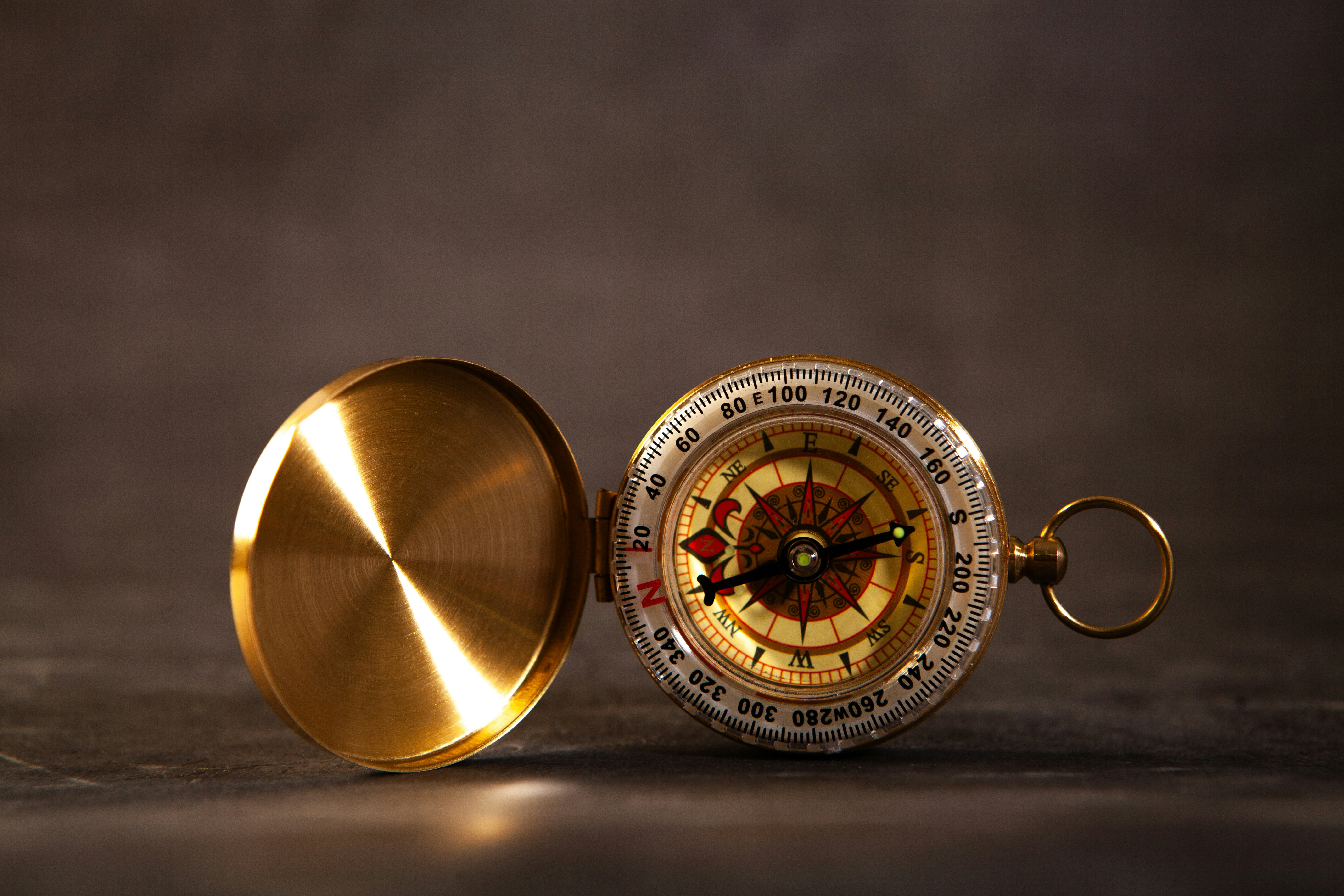 Antique brass compass with open lid on dark surface
