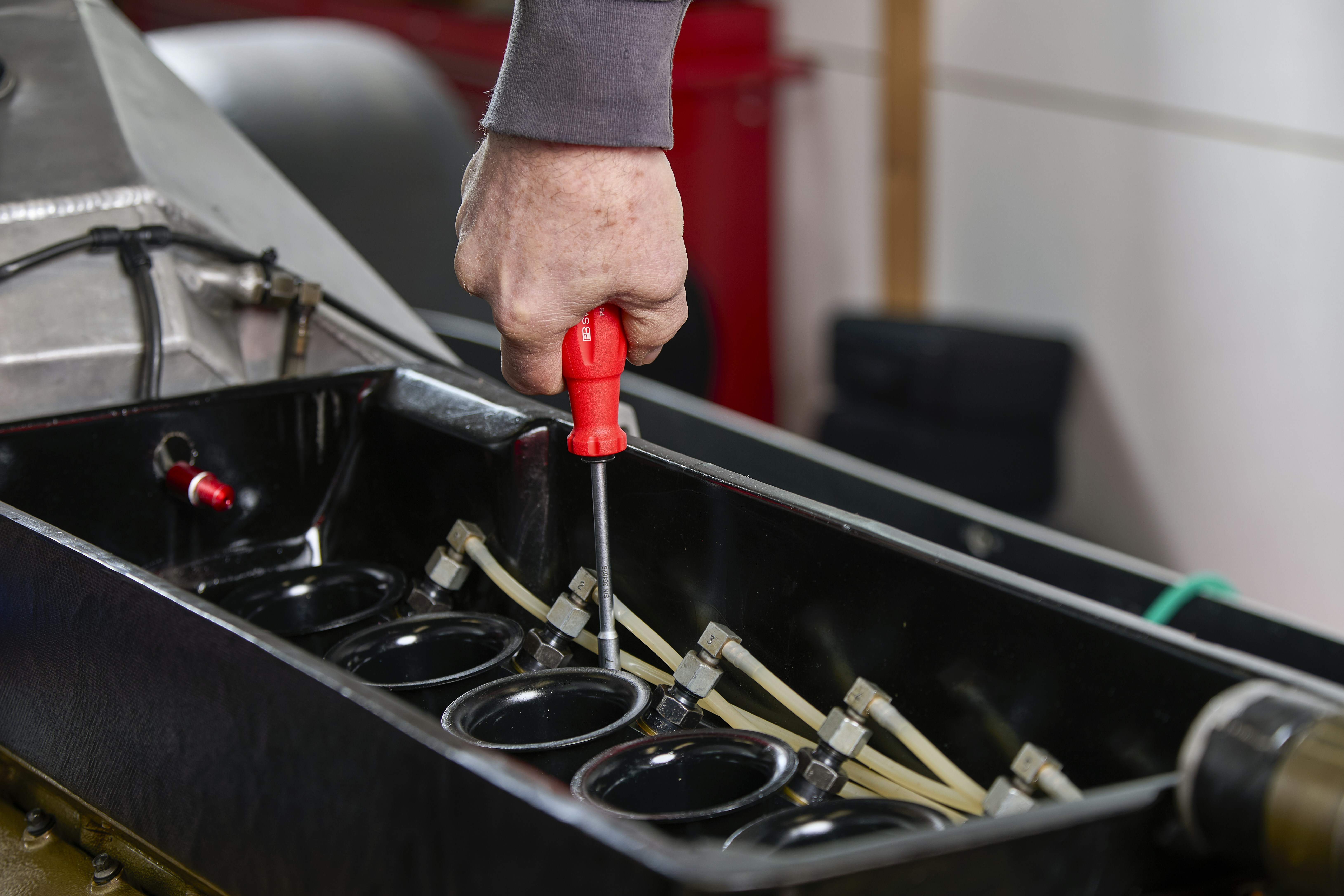 Mechanic using screwdriver on car engine components.