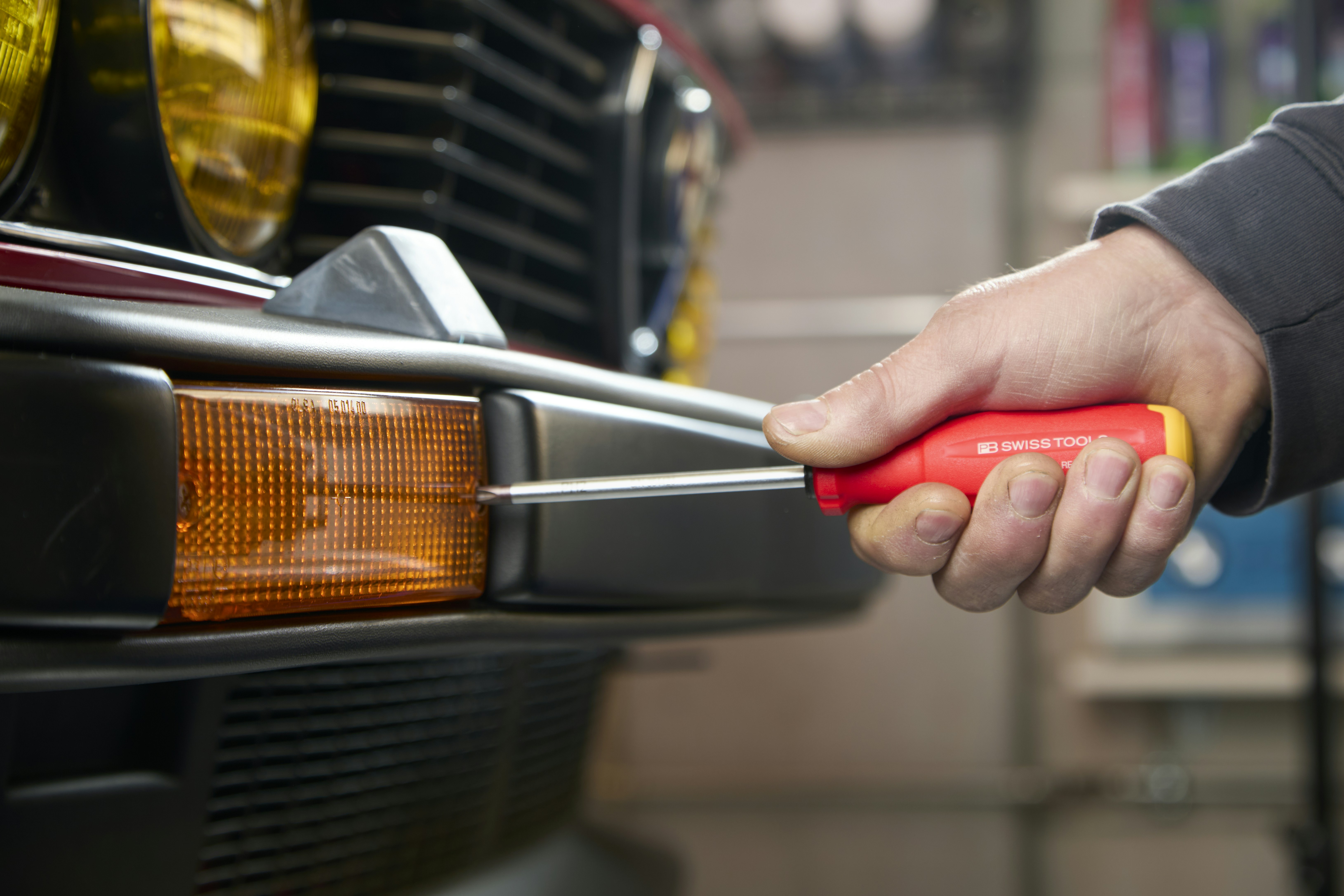 Hand using screwdriver on car bumper