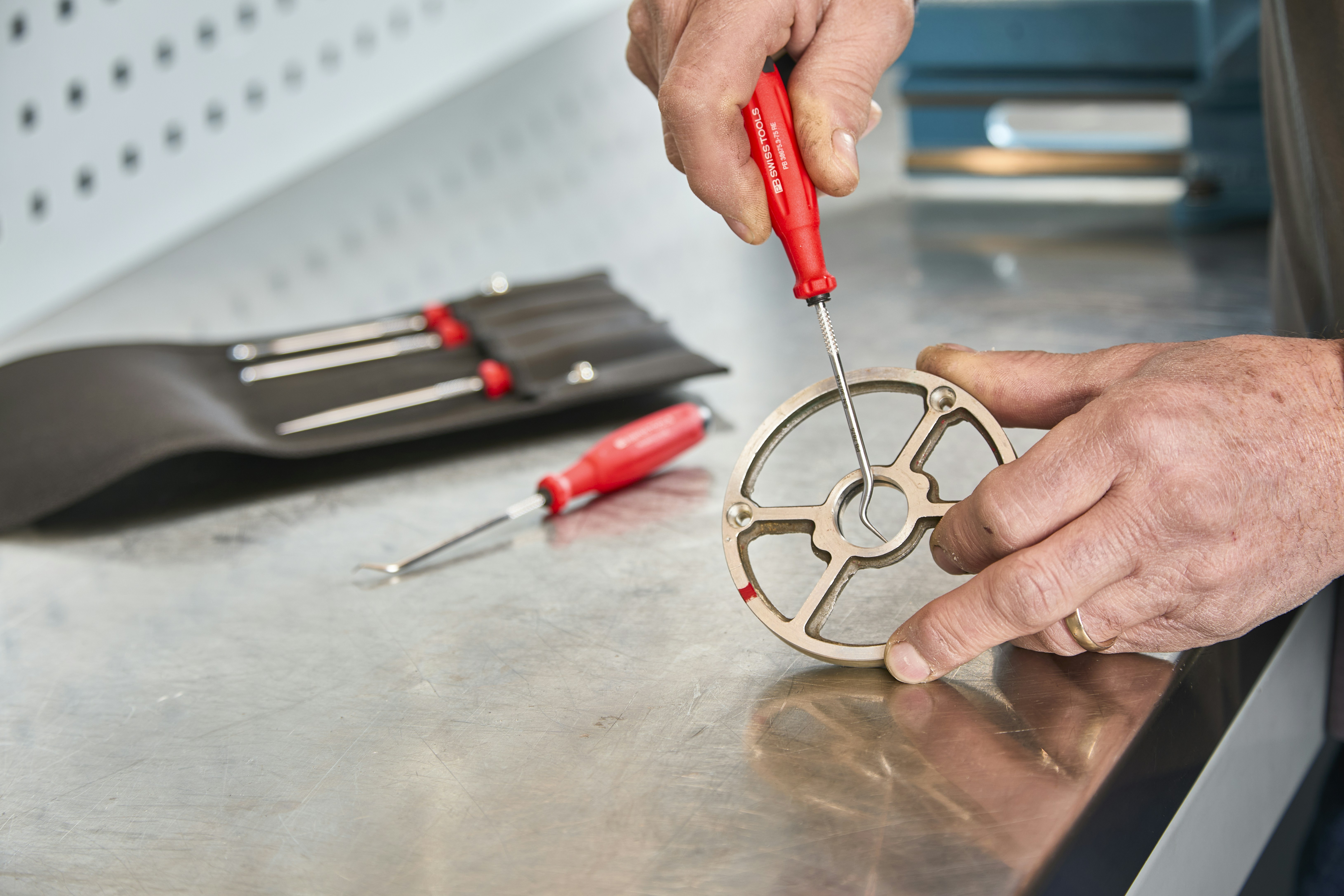 Hands using a screwdriver to fix a metal component.